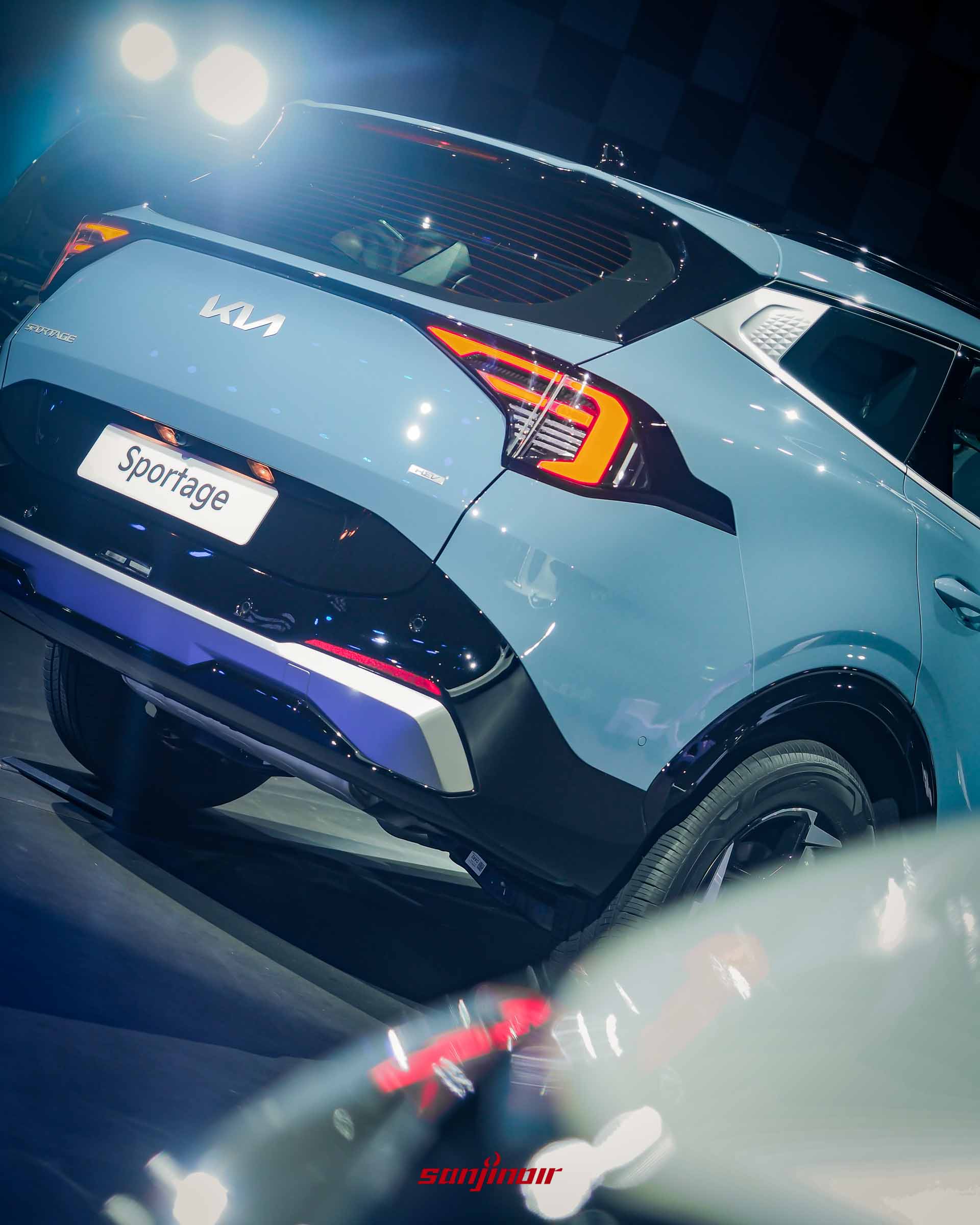 一台晨霧藍Kia Sportage的車尾近距離特寫，展示獨特的L型LED尾燈、全新KIA LOGO、車牌上的Sportage字樣，以及背景的格子牆和燈光。
