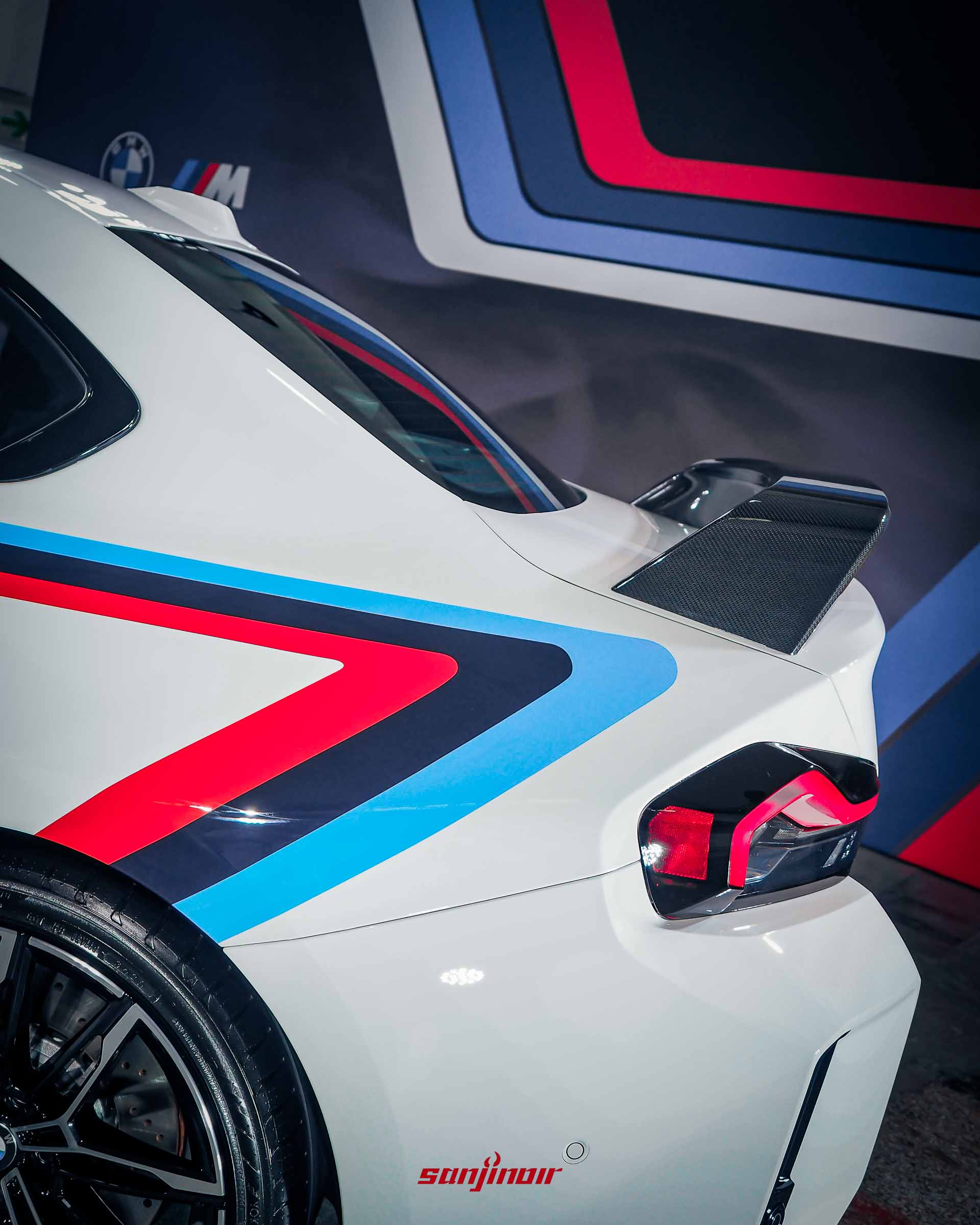 白色BMW M2車尾局部特寫照，聚焦於碳纖維擾流尾翼與C柱延伸至車尾的M三色烤漆線條。