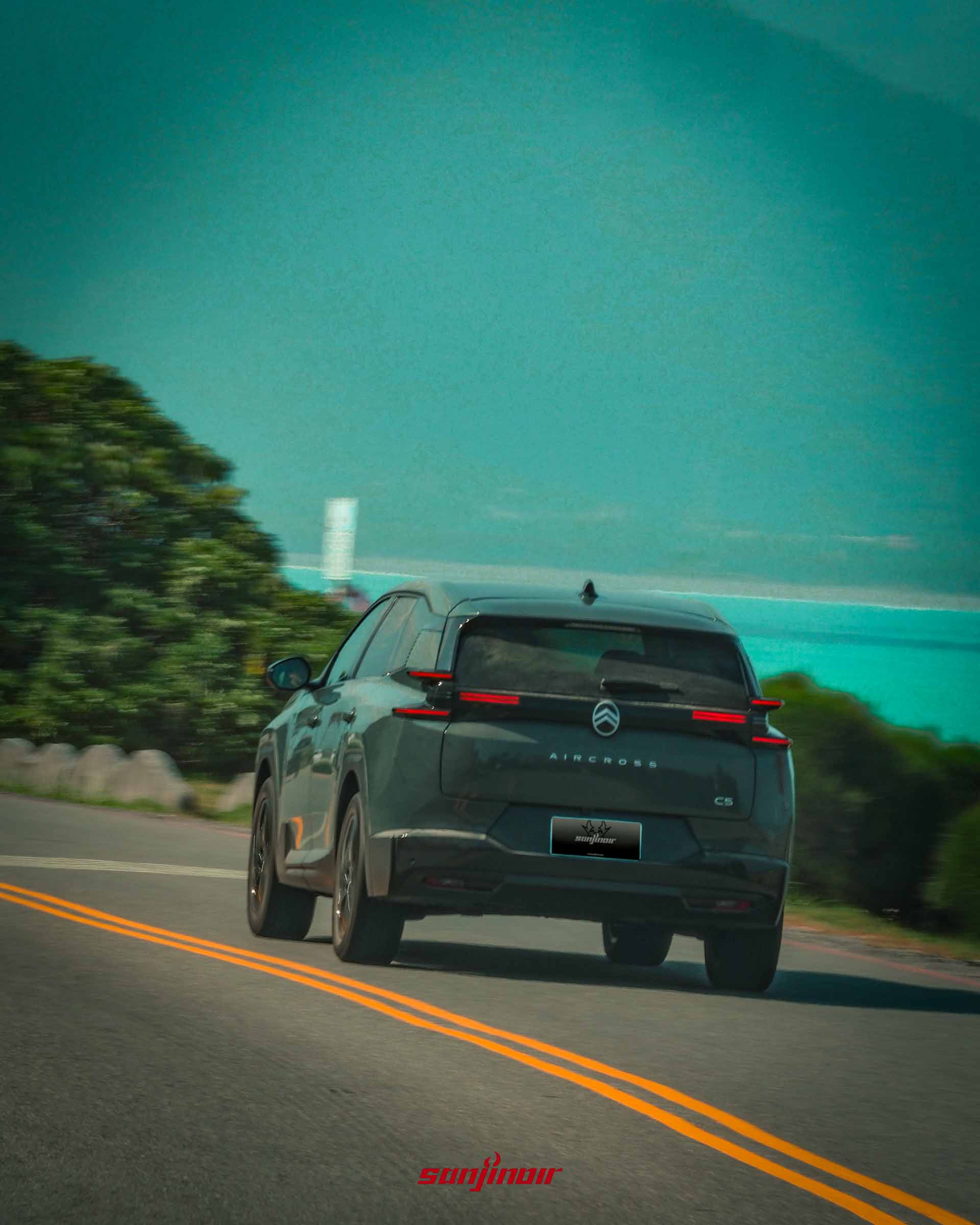 綠色CITROËN C5 Aircross行駛於海岸公路的車尾動態照,背景為藍色海洋與綠樹。