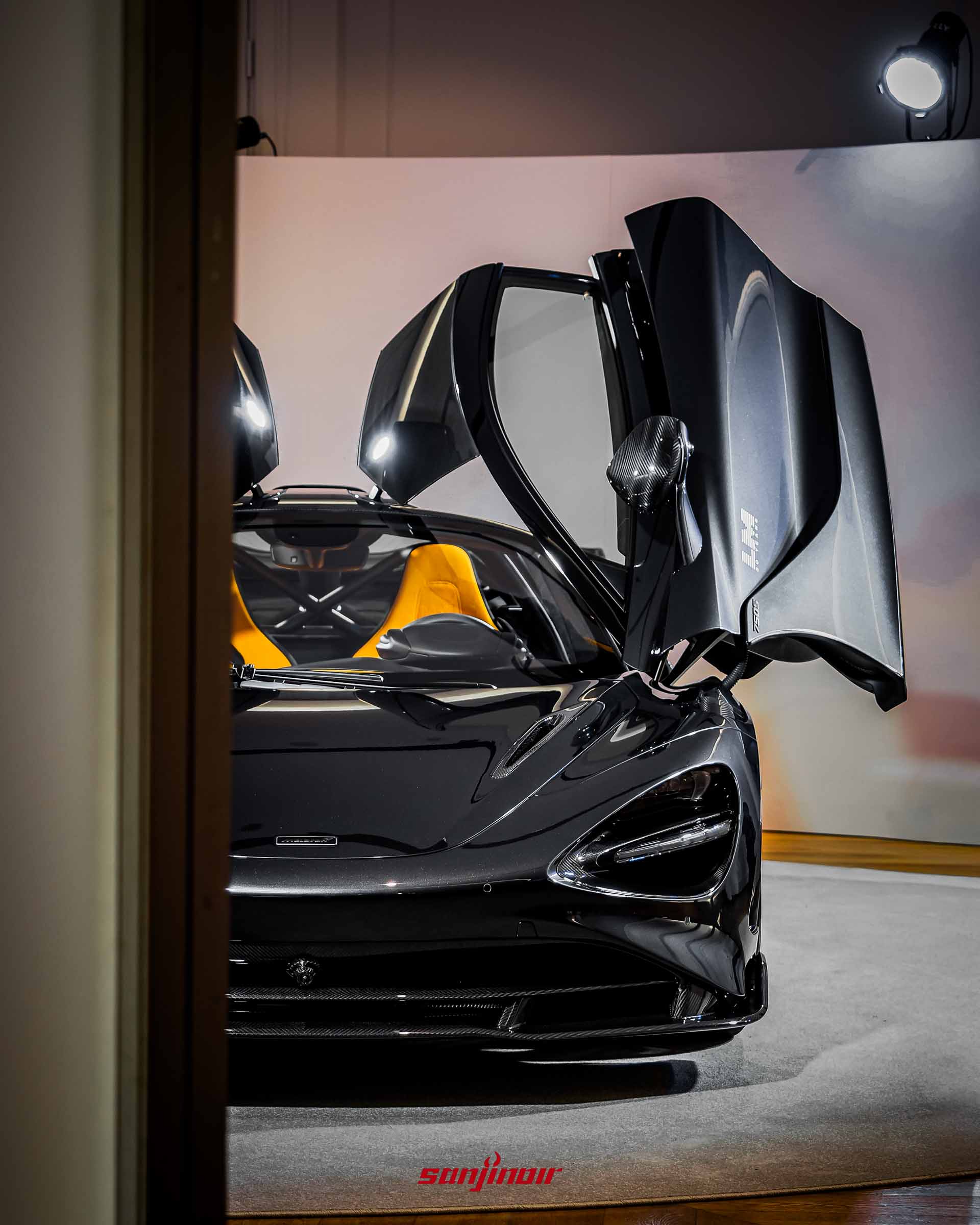 正面拍攝的McLaren 750S Le Mans,兩側蝶翼式車門向上展開,露出車內鮮豔的橘黃色賽車座椅與碳纖維細節。