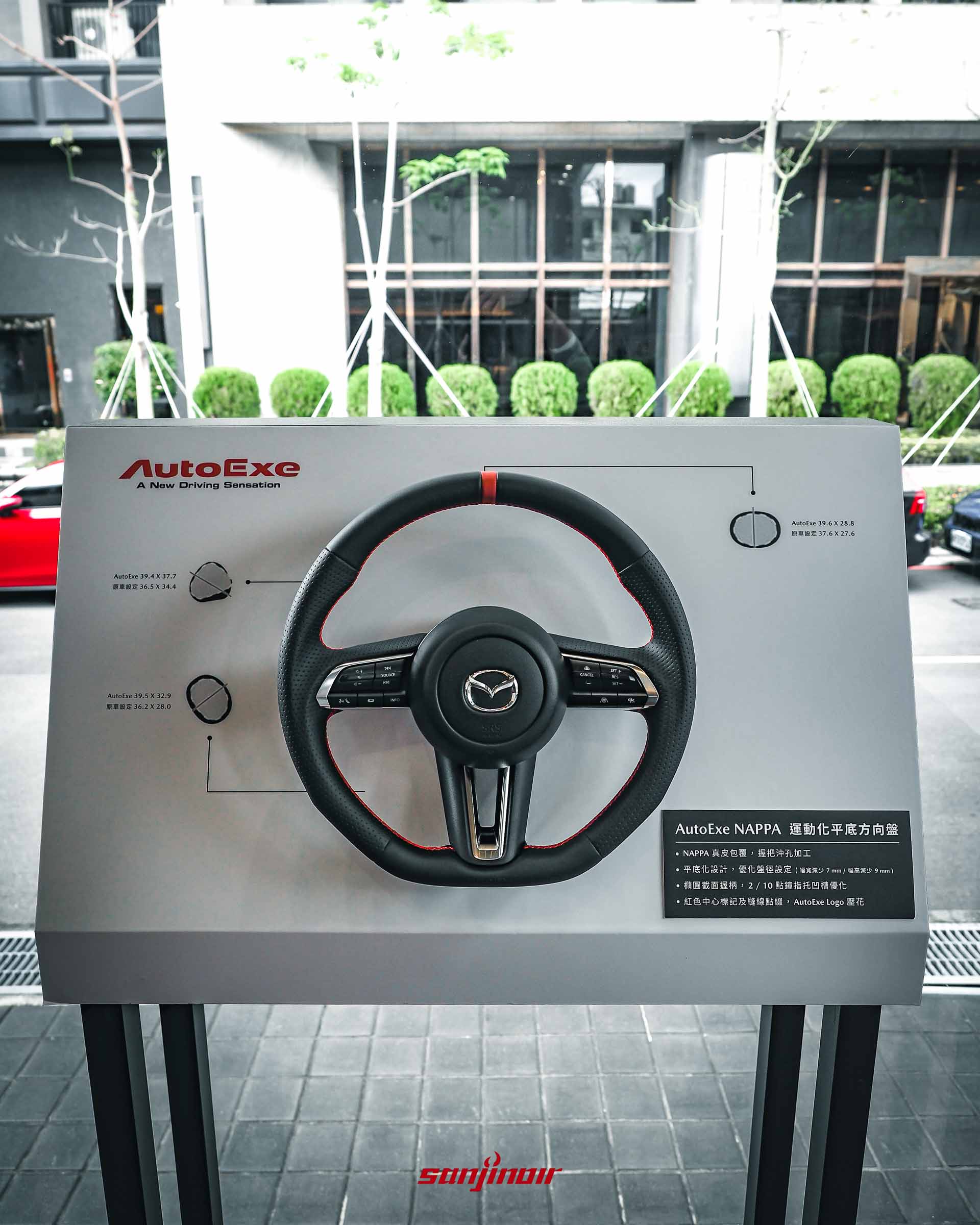 AutoExe 運動化平底方向盤展示架，背板說明其 NAPPA 真皮、縮小盤徑與武士刀柄指托等性能設計細節。