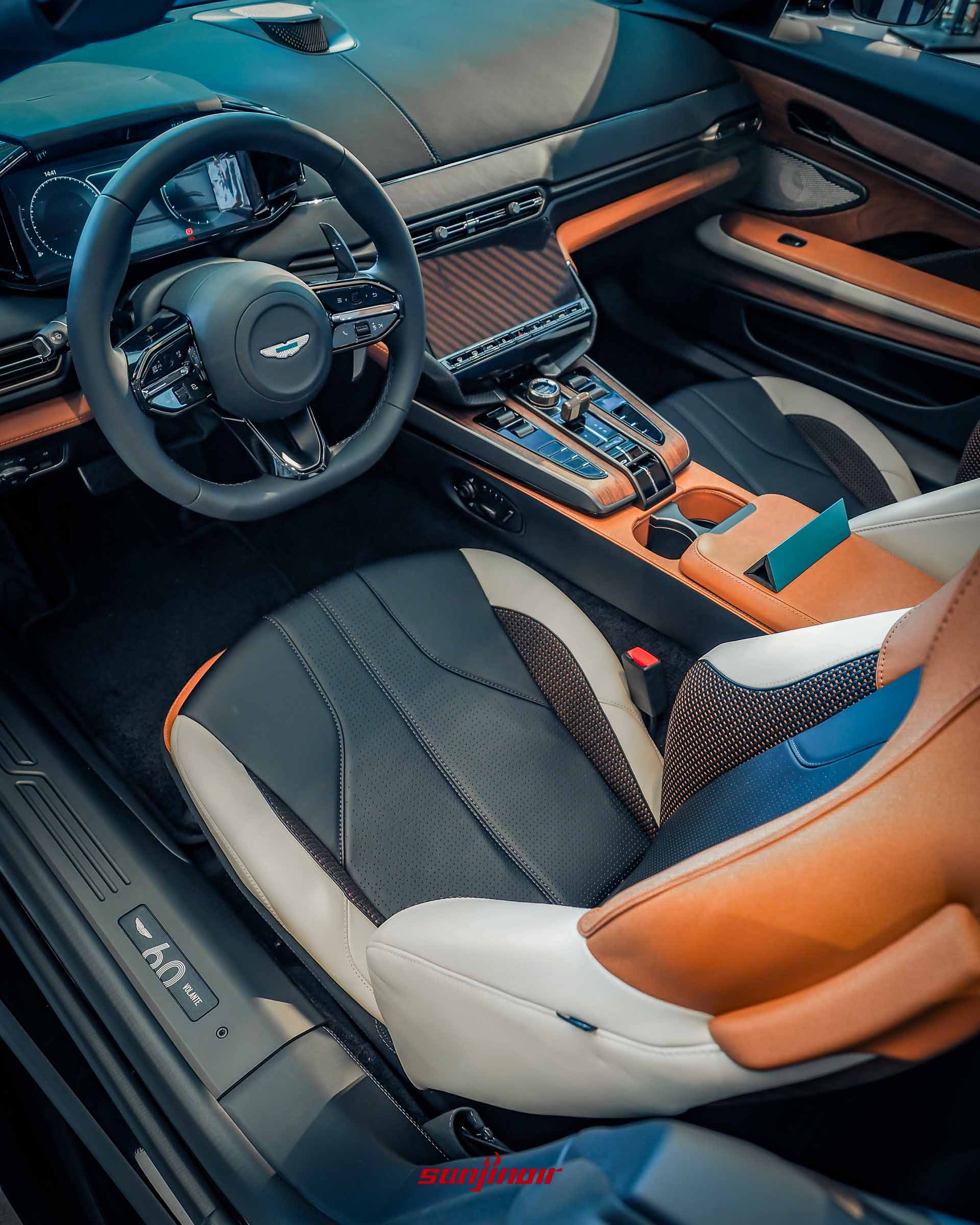 Vanquish Volante 60th Anniversary Edition 的內裝全景，軟頂收起。展示馬鞍棕與象牙白雙色編織皮革座椅，數位儀表板，中控觸控螢幕，古銅金金屬旋鈕，深色胡桃木飾板。門檻上有 60th Volante 徽飾。