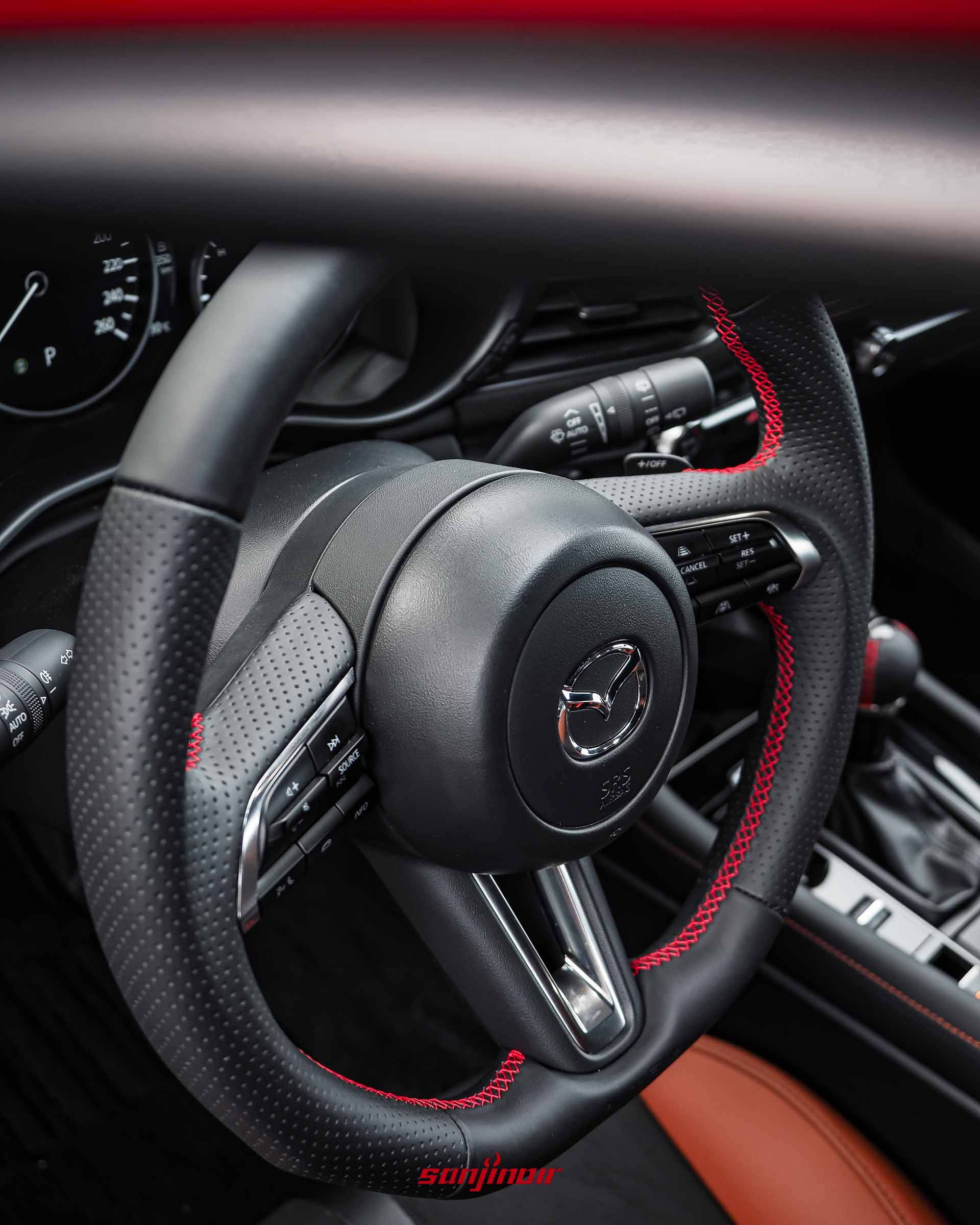 黑色AutoExe NAPPA運動化平底方向盤特寫，有沖孔、紅色中心標記和紅色縫線。