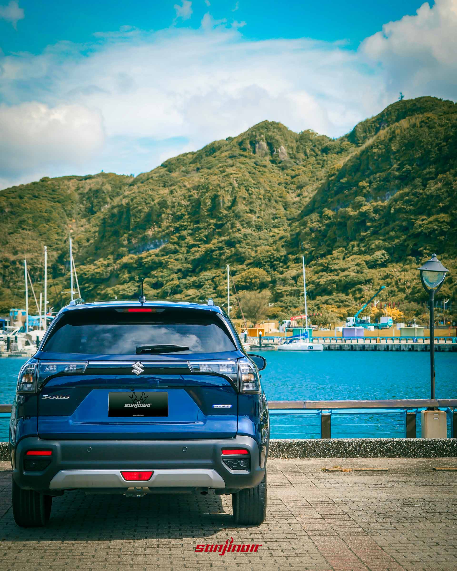 SUZUKI S-Cross Allgrip正車尾視角，背景為藍色海水與遠山。