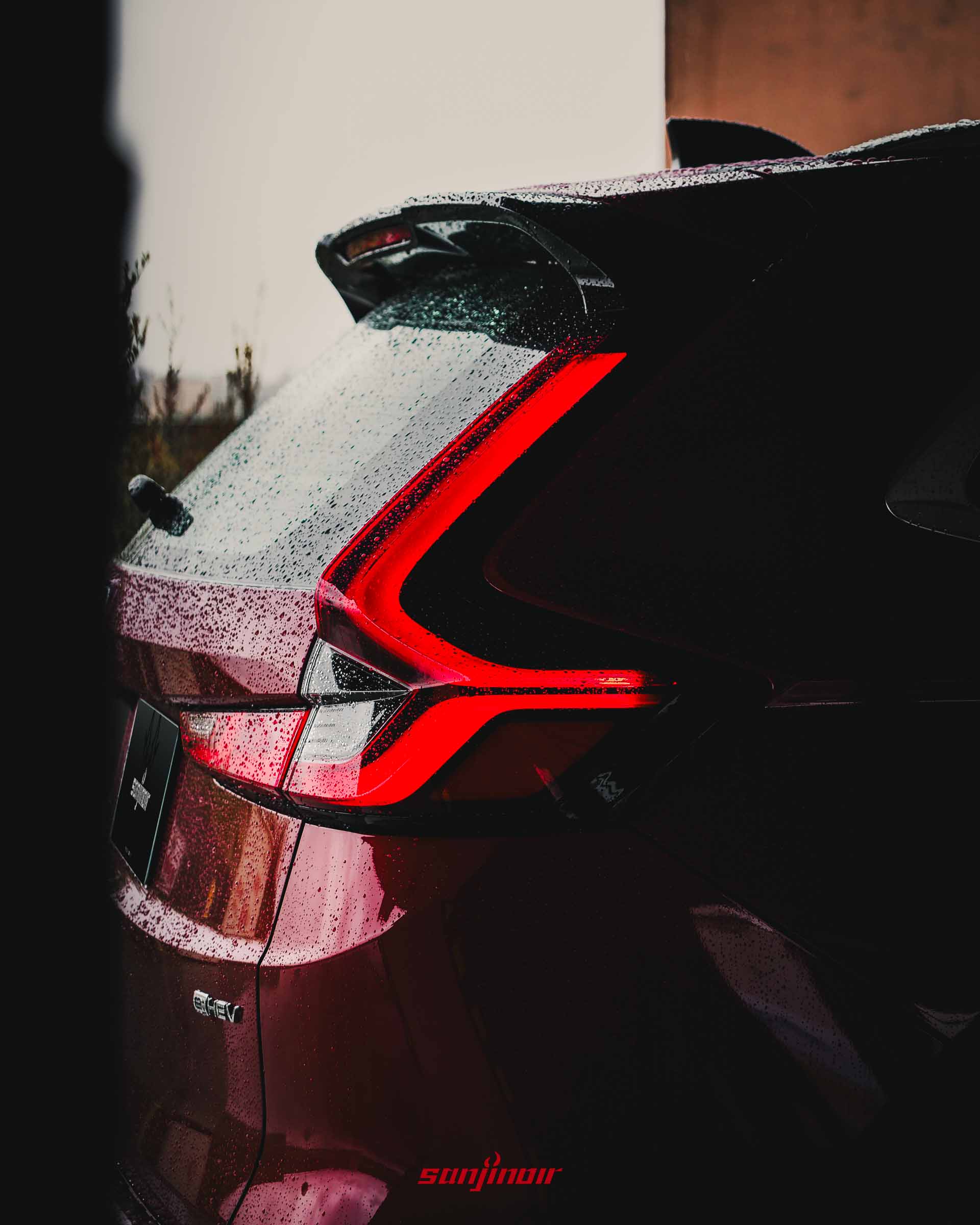 HONDA CR-V車尾L型LED尾燈的特寫鏡頭,車漆上佈滿雨水,邊緣可見鍍鉻的e:HEV字樣銘牌。