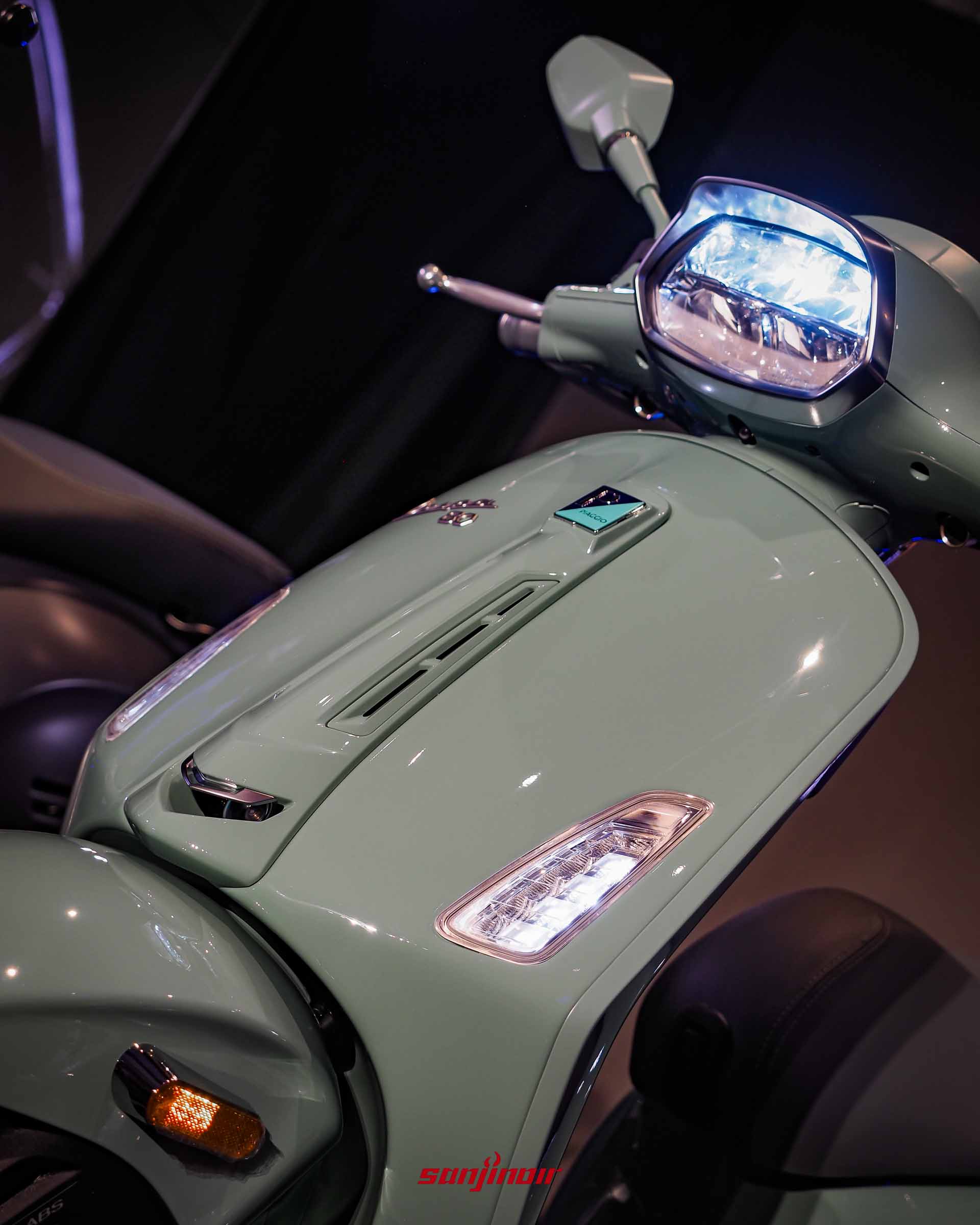 從斜上方俯拍綠色Vespa Sprint80周年特仕版車頭,展示亮起的頭燈與前面板流線造型。