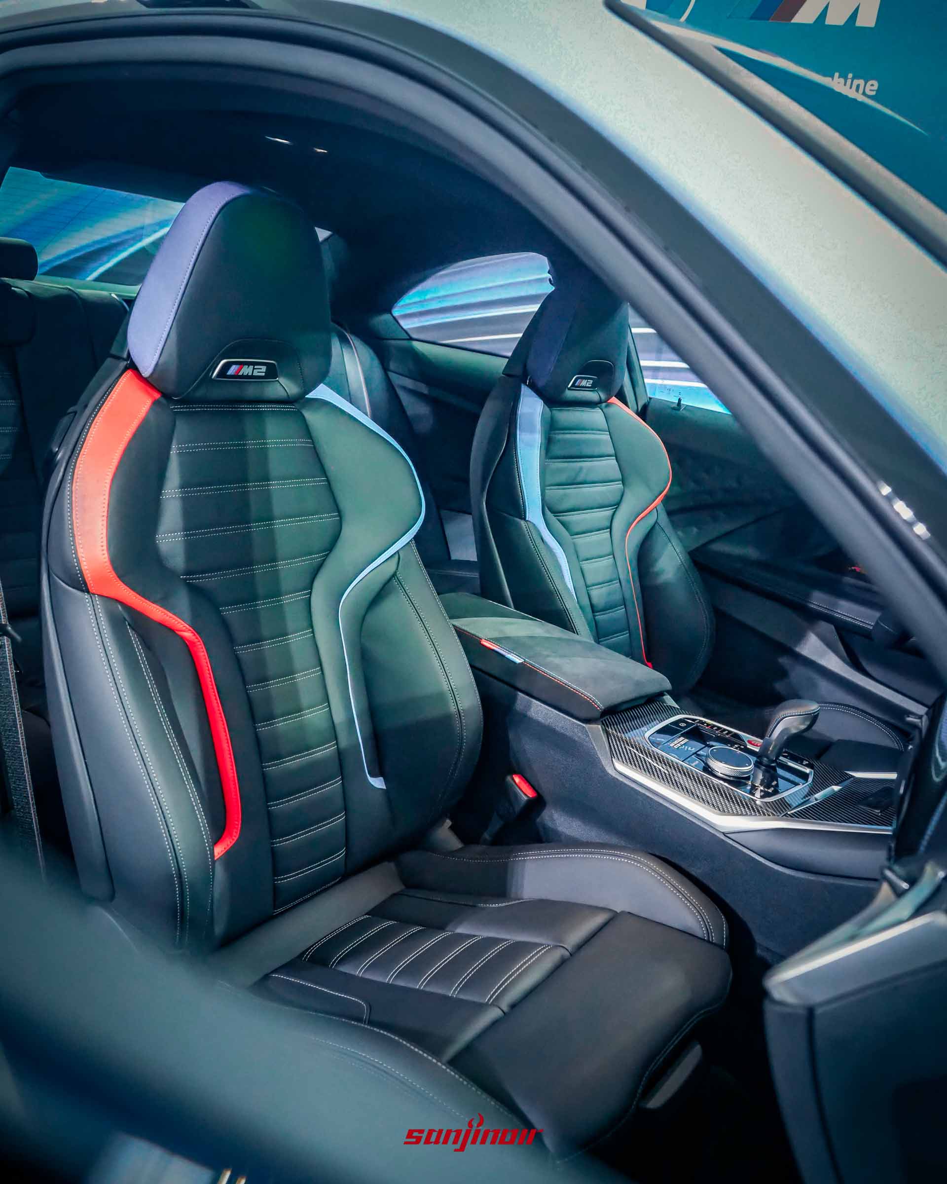 BMW M2車室內裝前排雙座特寫照，黑色皮革座椅帶有M三色專屬滾邊點綴，呈現強烈運動感。