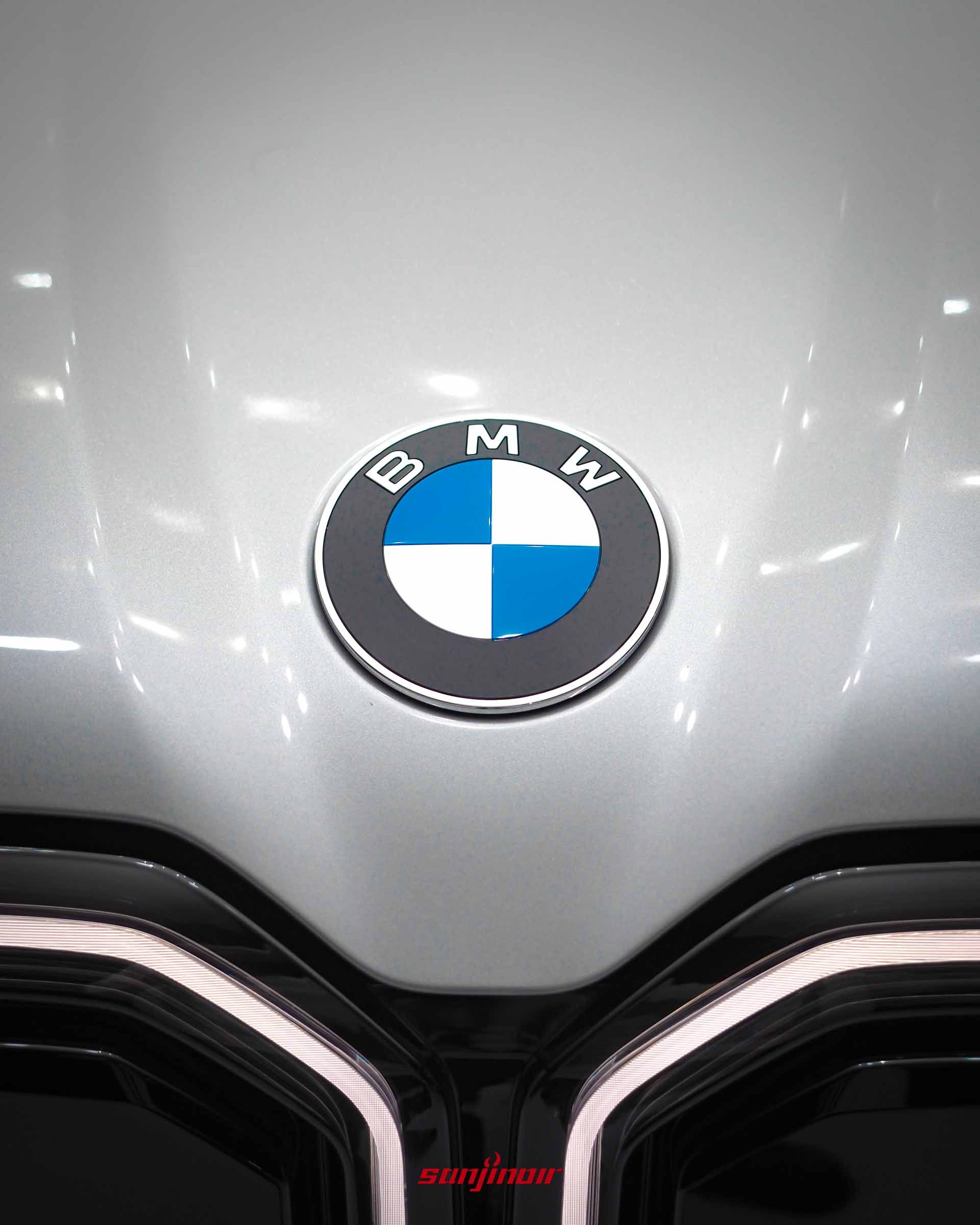 BMW iX3引擎蓋前端的藍白廠徽特寫,下方帶有微微凹陷的立體幾何折線。