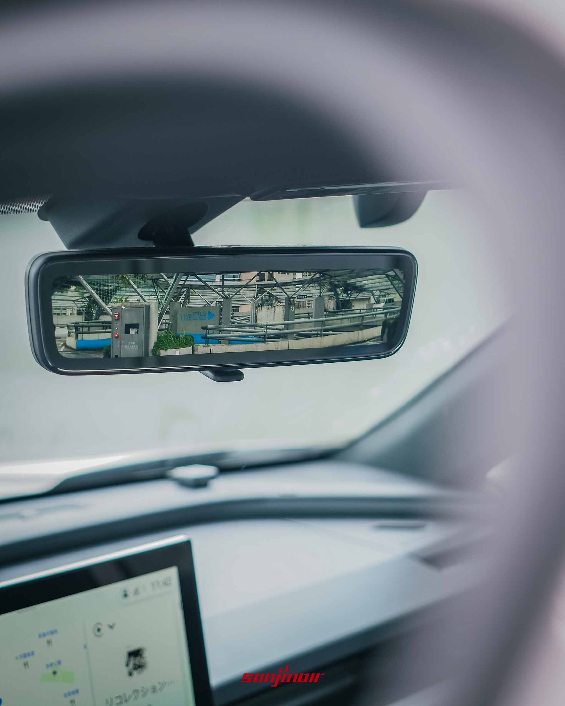 車內電子數位後視鏡特寫,鏡面螢幕清晰顯示著車後停車場的環境畫面。