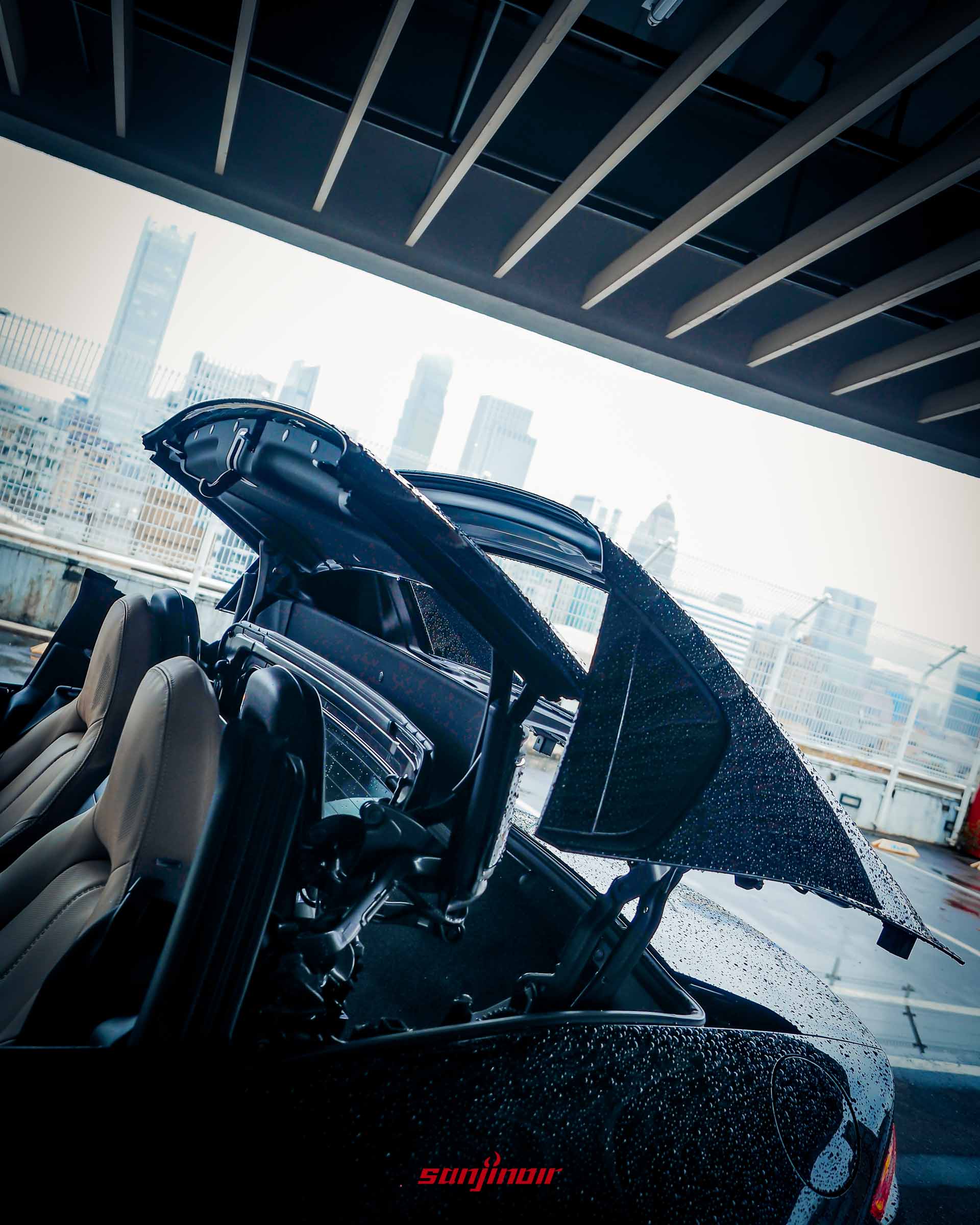 Mazda MX-5 RF 電動硬頂敞篷機構正在作動收折的瞬間特寫,車頂與後檔玻璃部分揚起,車身表面帶有水珠。