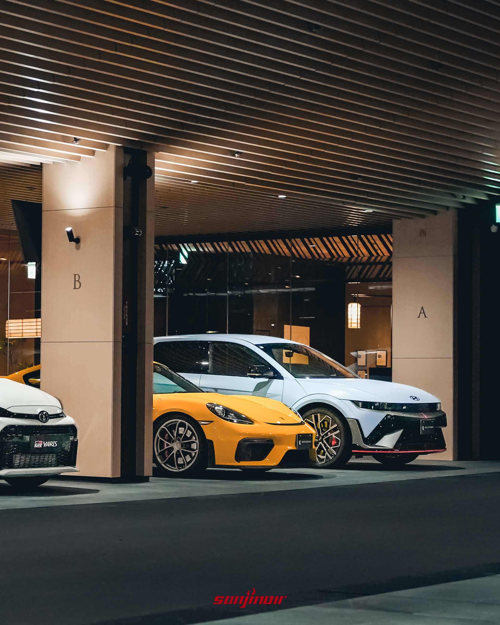 俱樂部半戶外停車區停放著白色 Toyota GR Yaris、黃色 Porsche 跑車以及淺藍色 Hyundai 性能電動車。