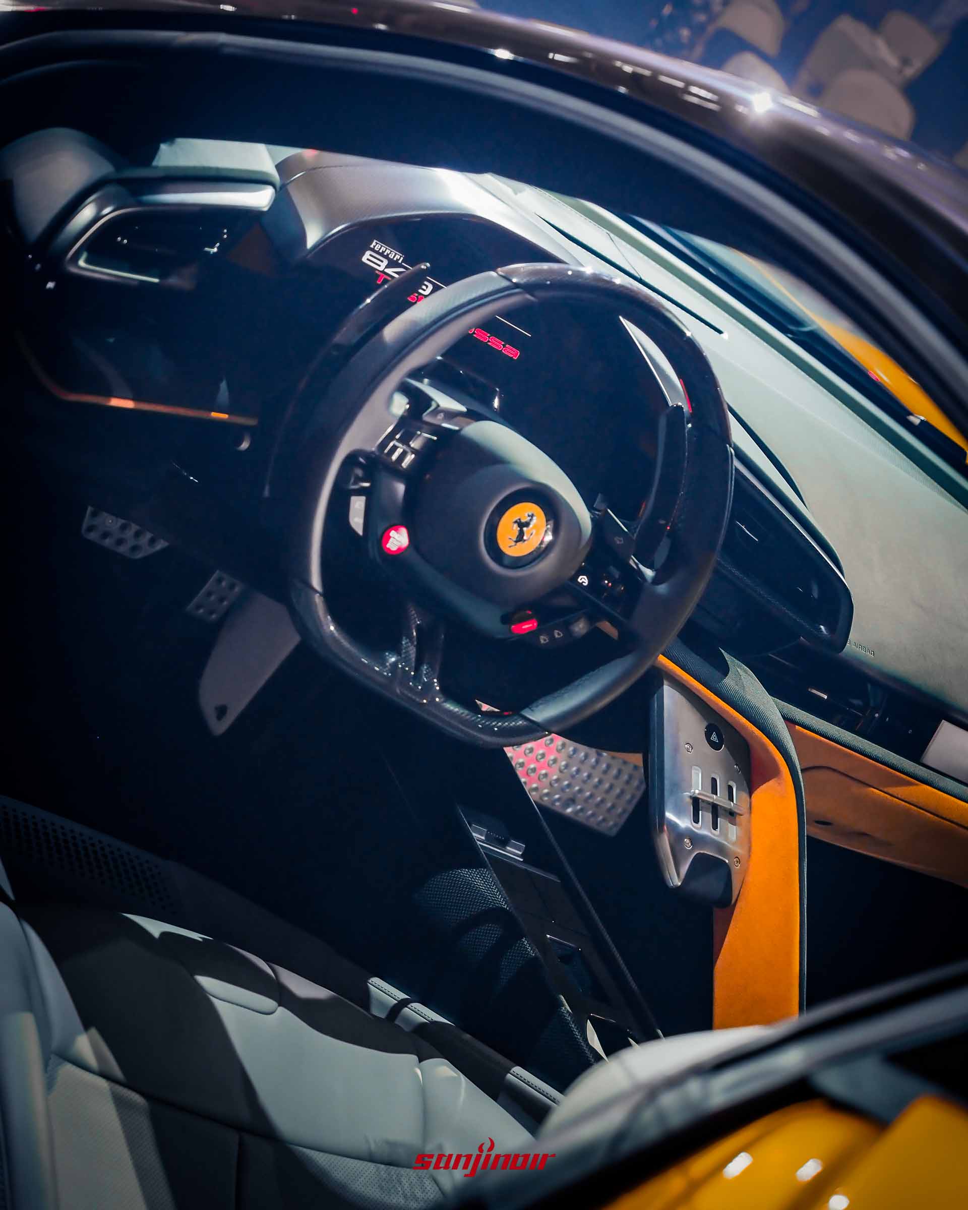 Ferrari 849 Testarossa 橙色車款的內裝，包括運動型方向盤 (上有躍馬標誌與多個按鈕)、數位儀表板與碳纖維結構。橙色的飾板點綴其中。