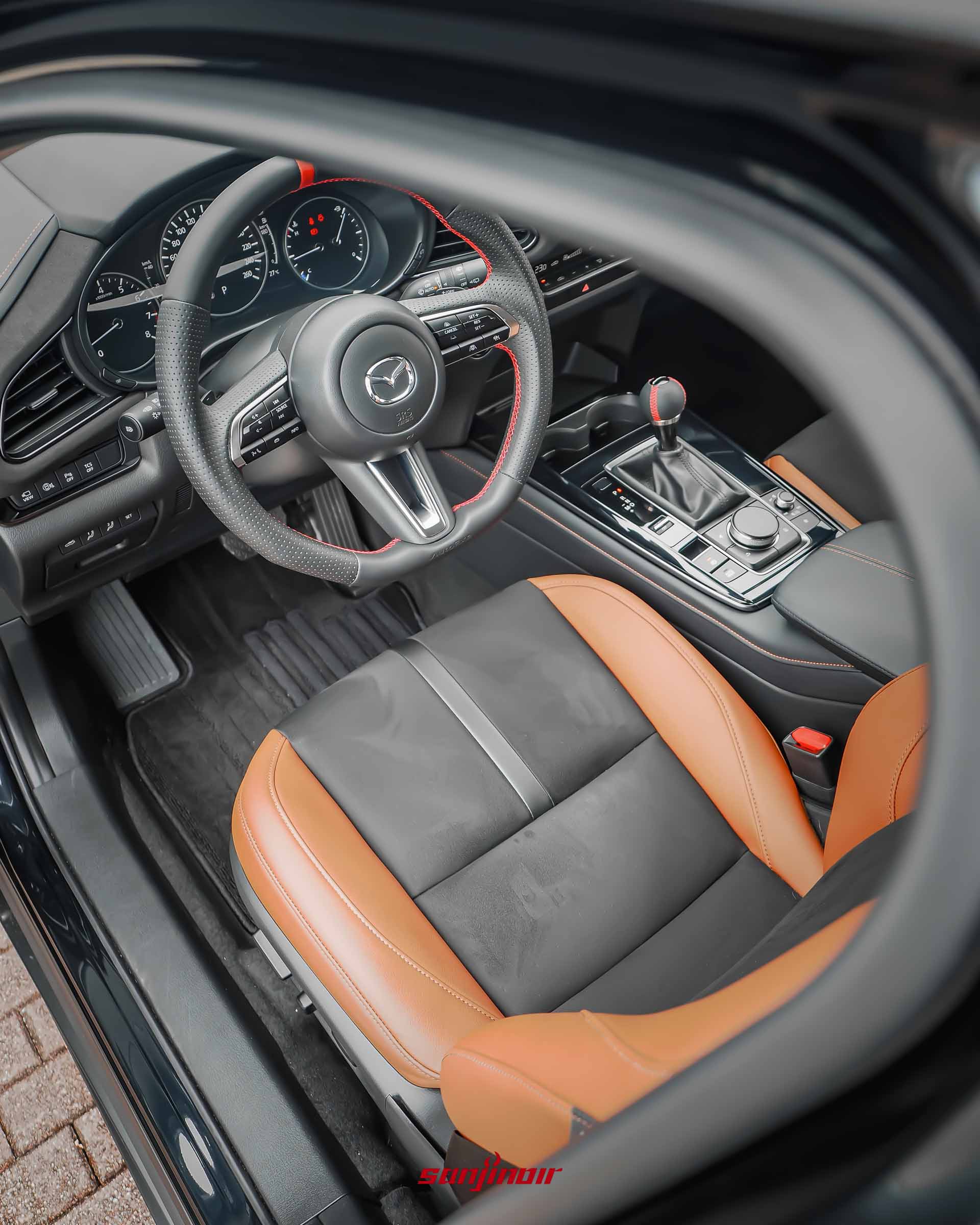 透過開啟的車窗拍攝MAZDA CX-30 20S Homura內裝,展示AutoExe方向盤、排檔桿及雙色麂皮運動化座椅。