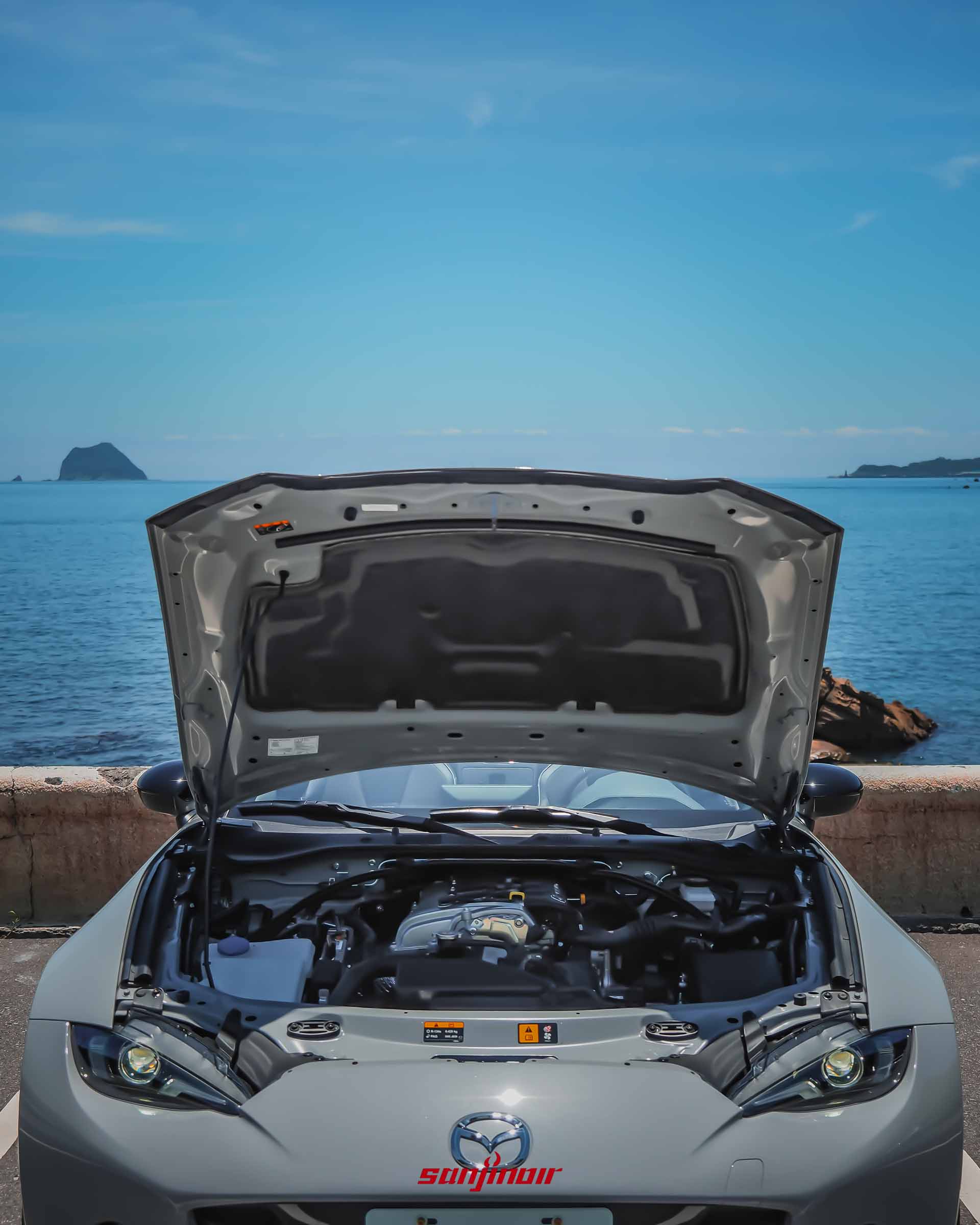 灰色MAZDA MX-5 RS停放於海邊,引擎蓋呈開啟狀態,展露其縱置直列四缸引擎本體與引擎室配置。