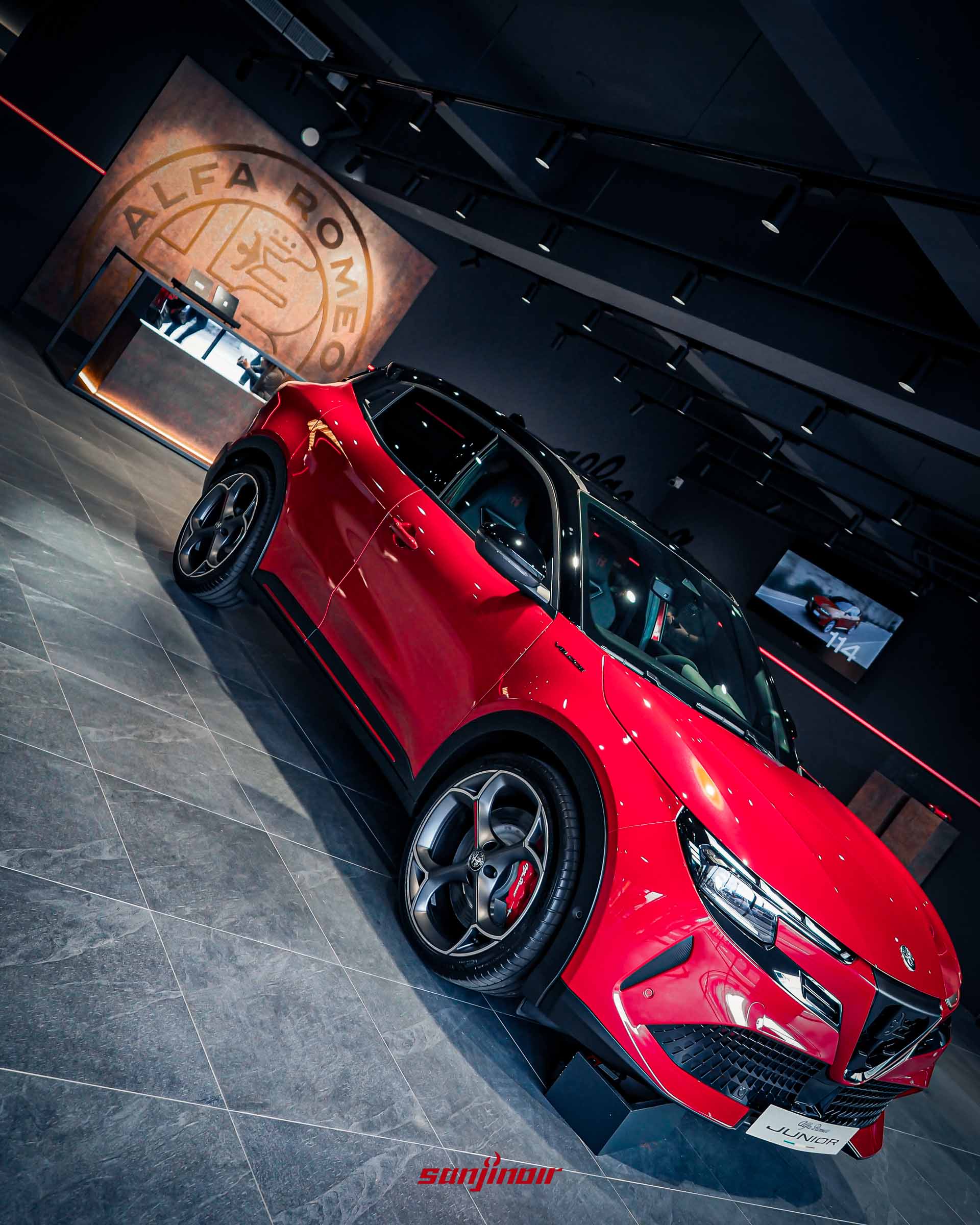 2026台北車展性能焦點紅色Alfa Romeo Junior Veloce車側後方45度角全身照，背景為品牌Logo牆。