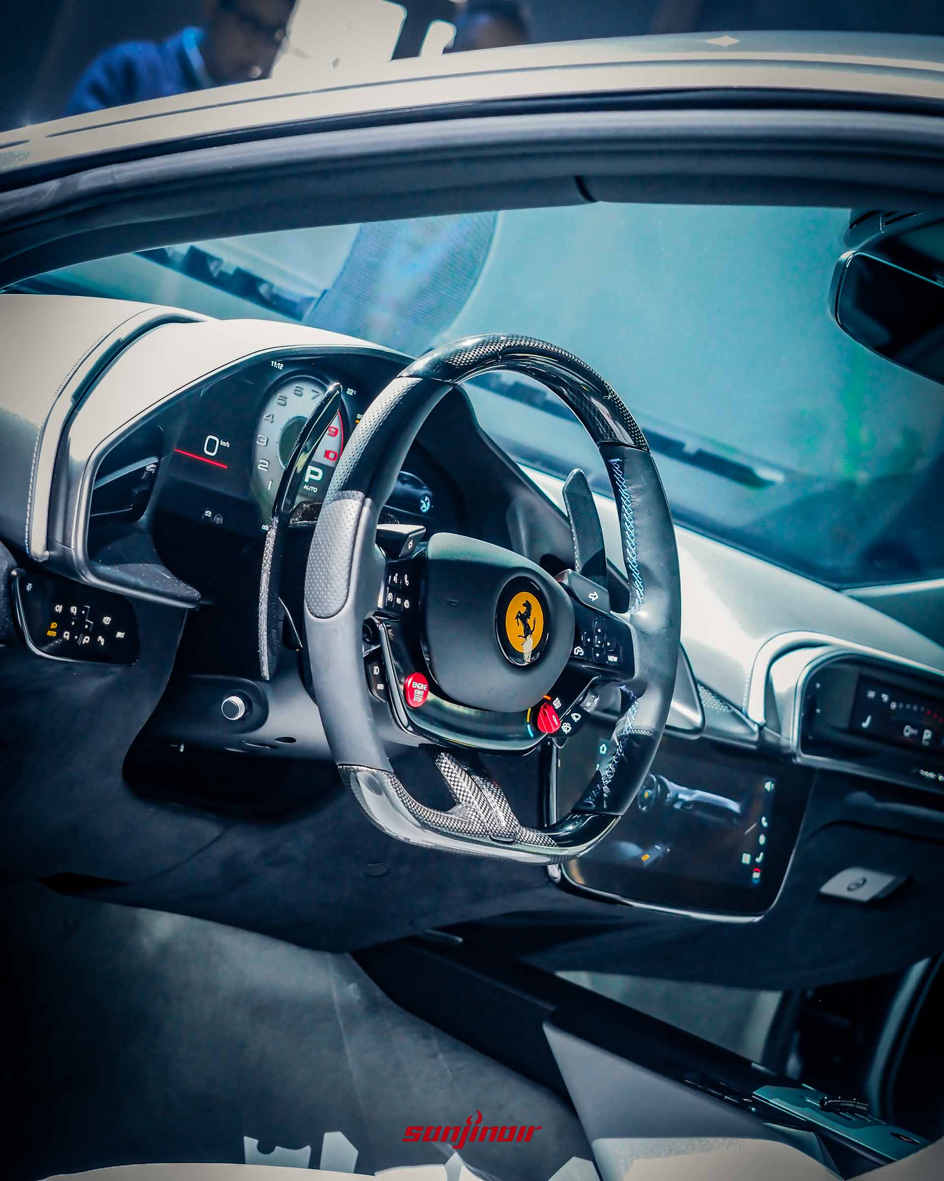 Ferrari Amalfi駕駛座艙視角，展示碳纖維方向盤、實體啟動按鈕、換檔撥片及全數位儀錶板。