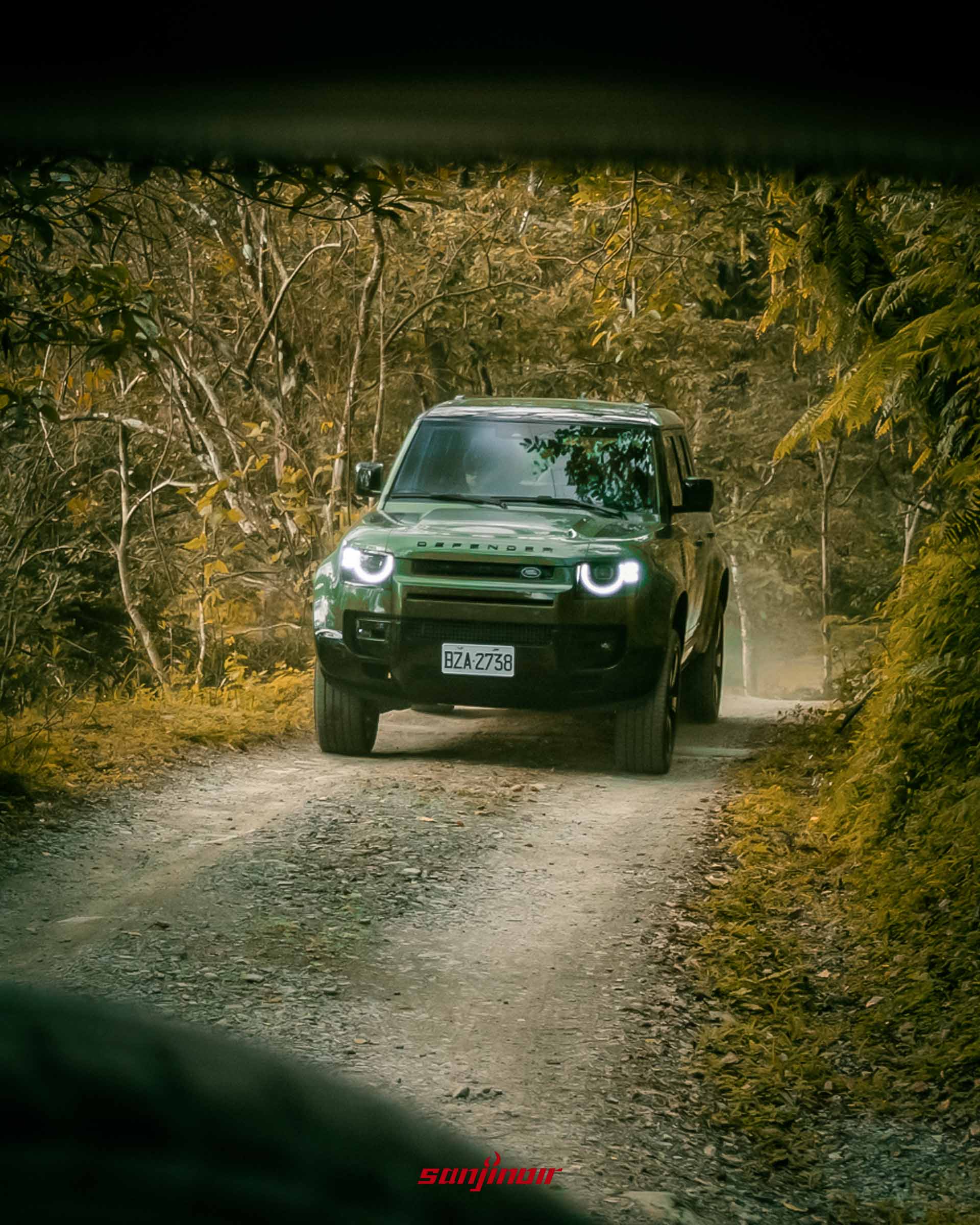 綠色Defender行駛於狹窄林間泥地車頭LED頭燈亮起。