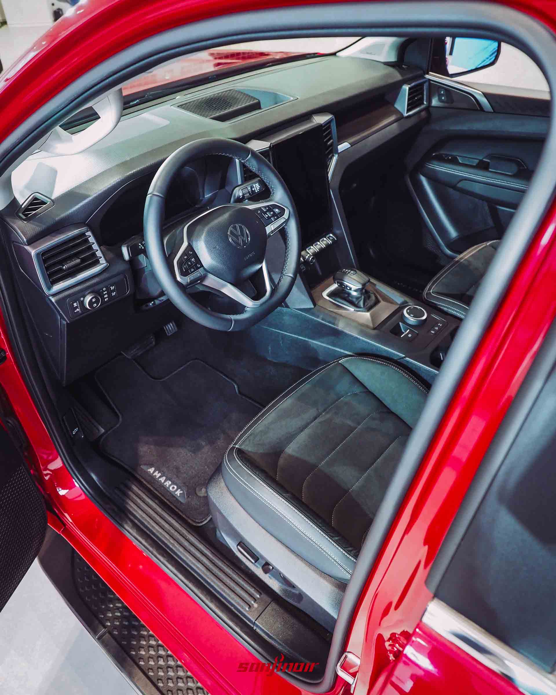 由駕駛座車門外向內拍攝的內裝全景，包含多功能方向盤、數位儀表板、大尺寸中控螢幕與質感座椅。