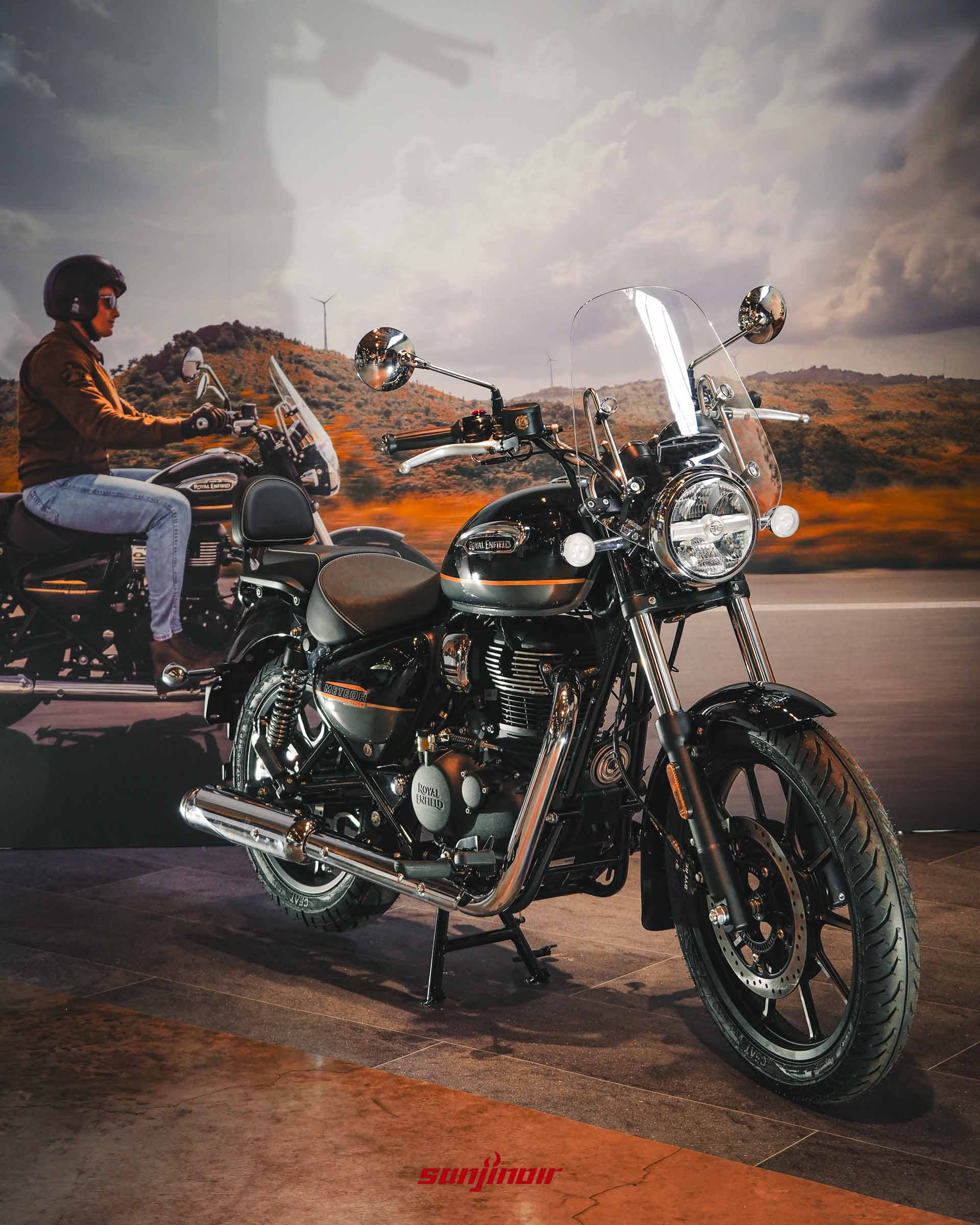 Royal Enfield Meteor 350摩托車展示，黑色車身配有橘色拉線與單座墊，背景為騎士騎乘圖案。