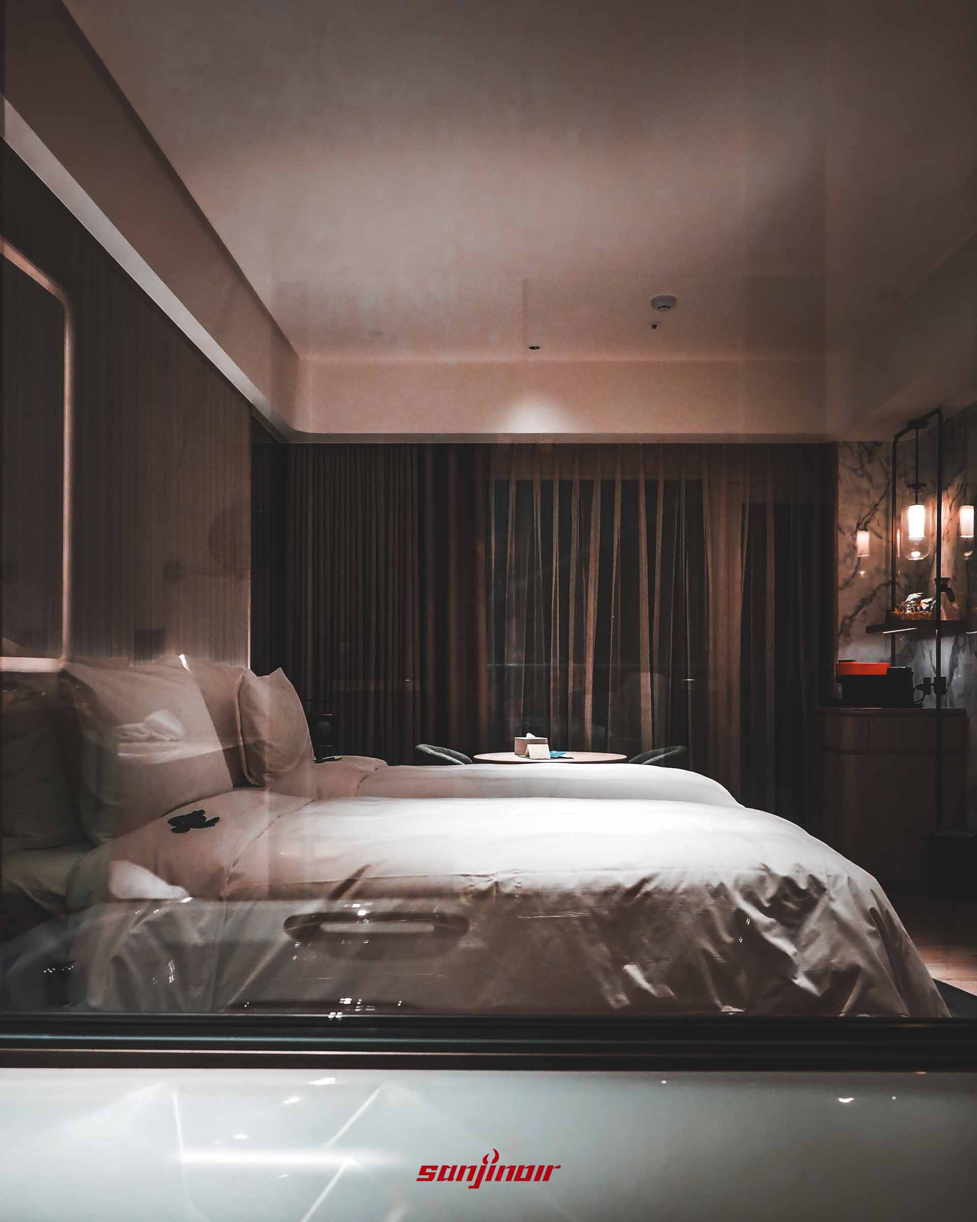 透過玻璃拍攝的客房內部,設有兩張床鋪與落地窗簾。