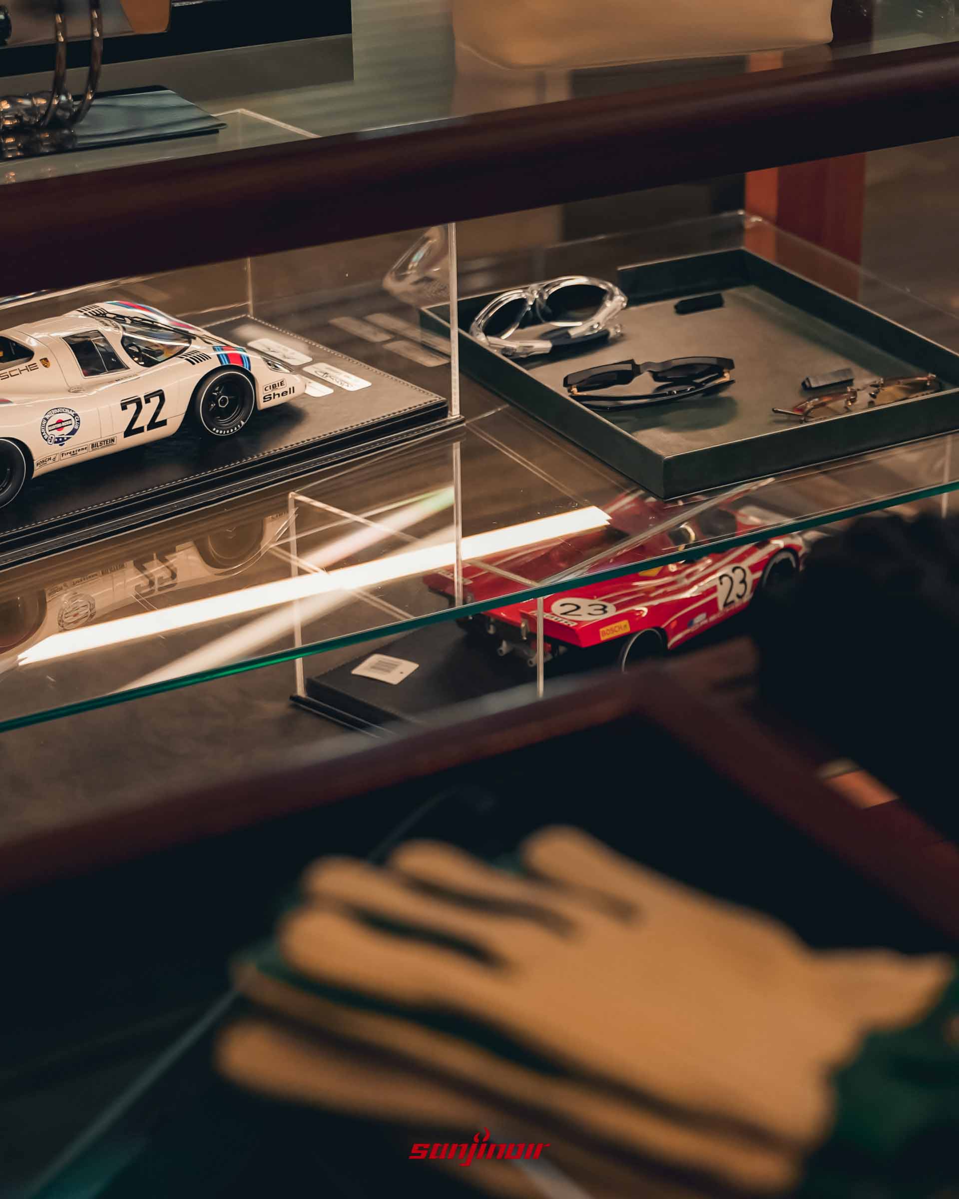 玻璃展示櫃內擺放著 Porsche 與 Ferrari 等經典賽車的縮小模型，以及護目鏡與賽車手套等部品。