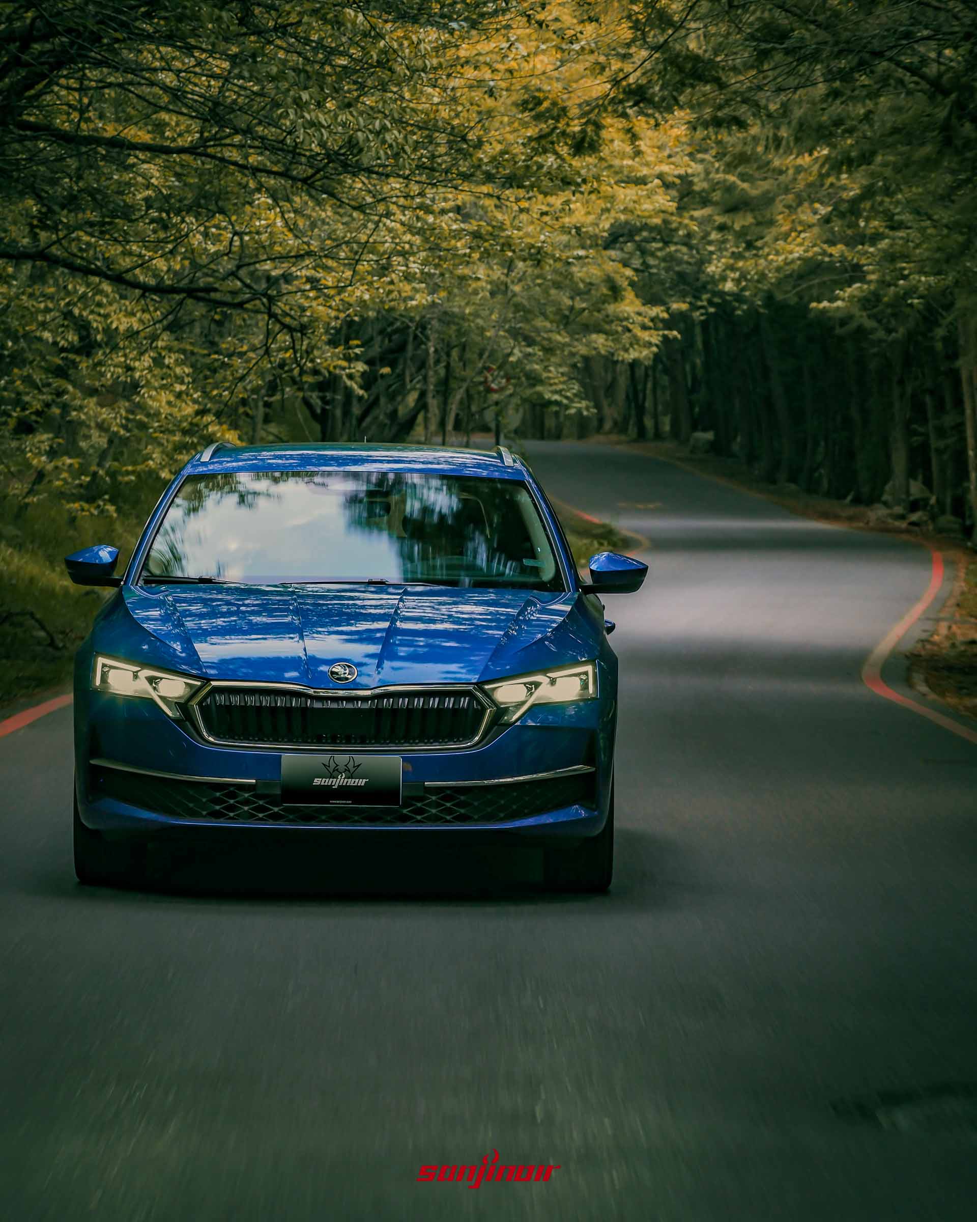 藍色 Škoda Octavia Combi 2.0 TSI 4×4 駛入有著紅色邊線的蜿蜒山林道路，兩旁種滿茂密的綠色樹木。