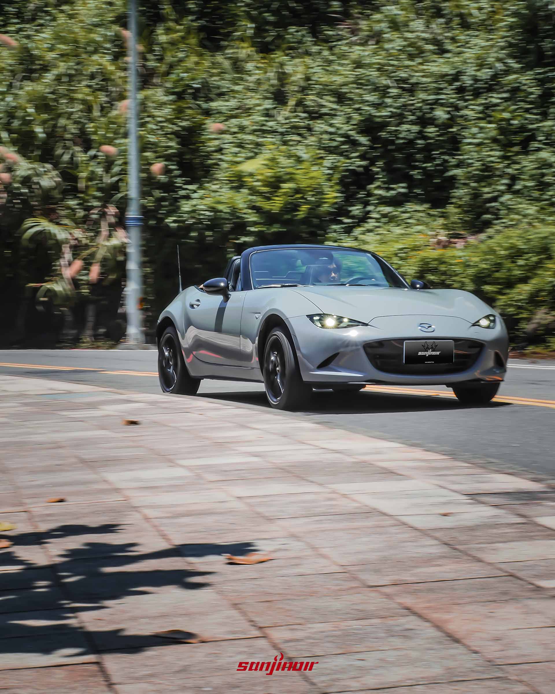 動態追焦攝影,灰色MAZDA MX-5 RS於樹影婆娑的公路上行駛,呈現動感的開篷姿態。