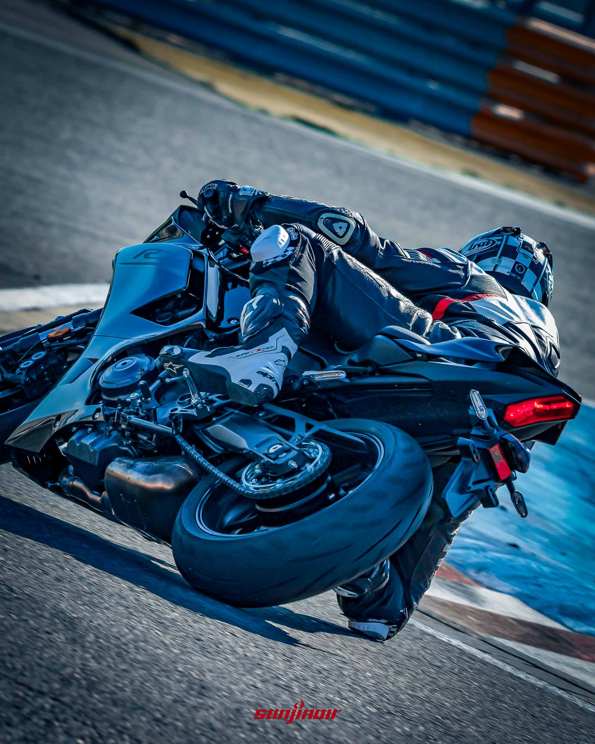 一名穿著連身防摔衣的騎士,正駕駛黑色Yamaha YZF-R7在賽道上向右壓車過彎,視角由車尾斜後方捕捉。