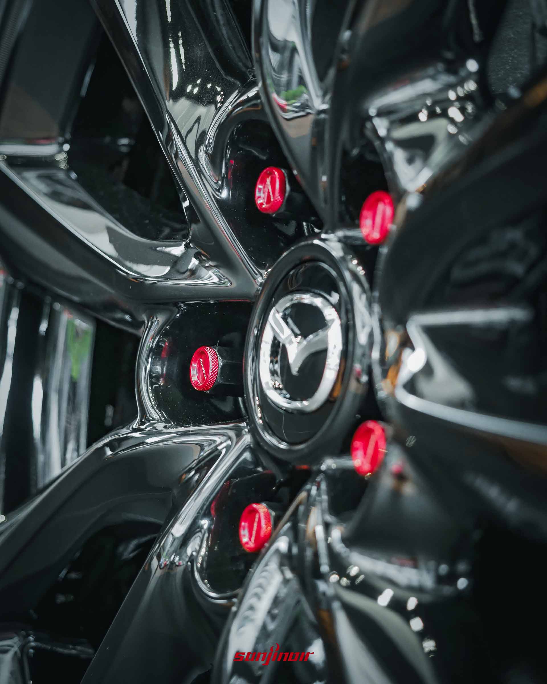MAZDA 車輛爍黑鋁合金輪圈特寫，輪框上安裝了醒目的 AutoExe 湛紅高剛性防盜螺帽，展現紅黑對比的改裝跑格。