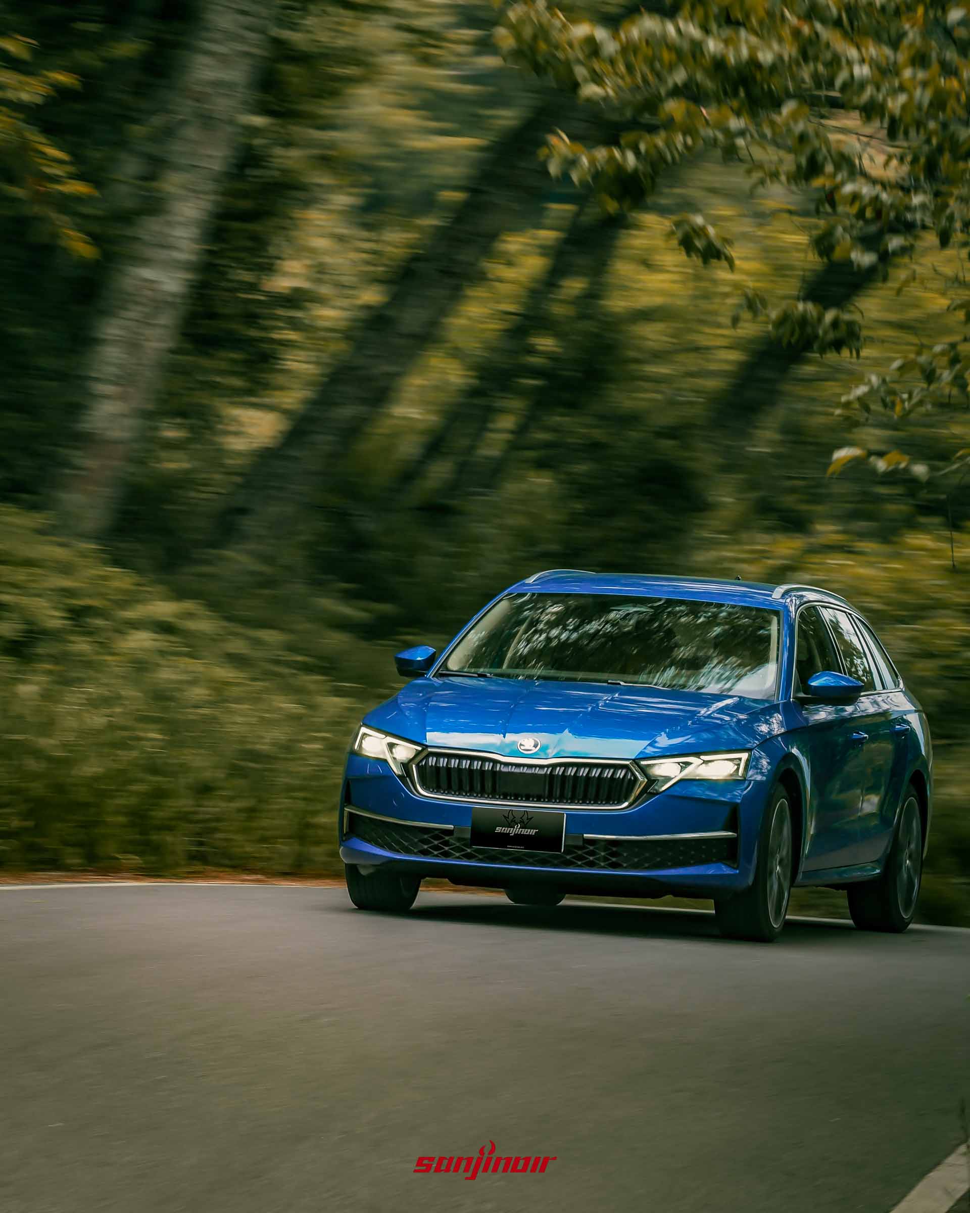 藍色 Škoda Octavia Combi 2.0 TSI 4×4 在山路過彎時的追焦攝影照片，背景樹叢模糊以強調車輛的過彎動態。