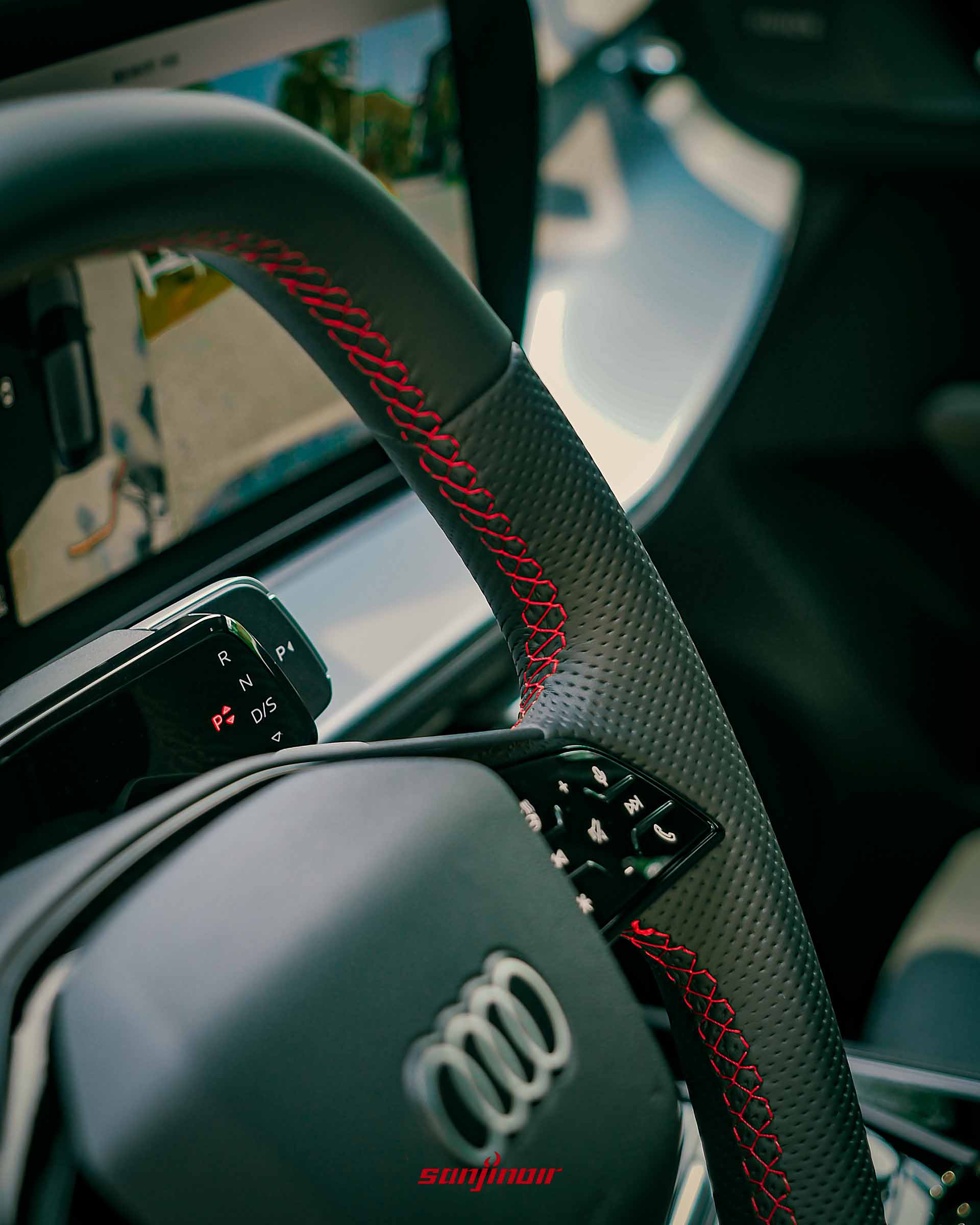 Audi Q3方向盤特寫，展示紅色縫線、全新線傳排檔與後方中央觸控螢幕細節。