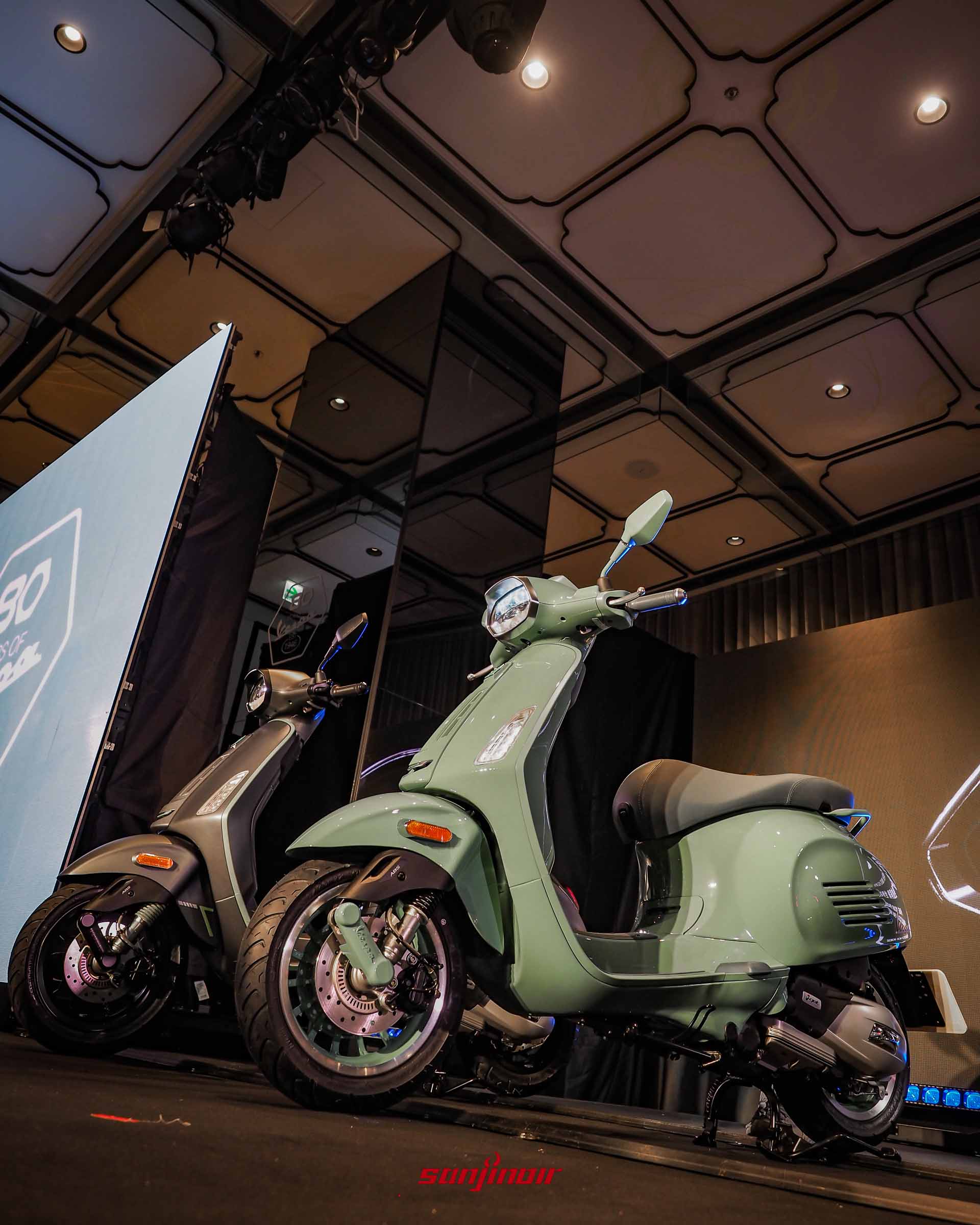 發表會舞台上並列的兩台綠色Vespa Sprint80周年特仕版,上方投射藍色與白色的舞台燈光。