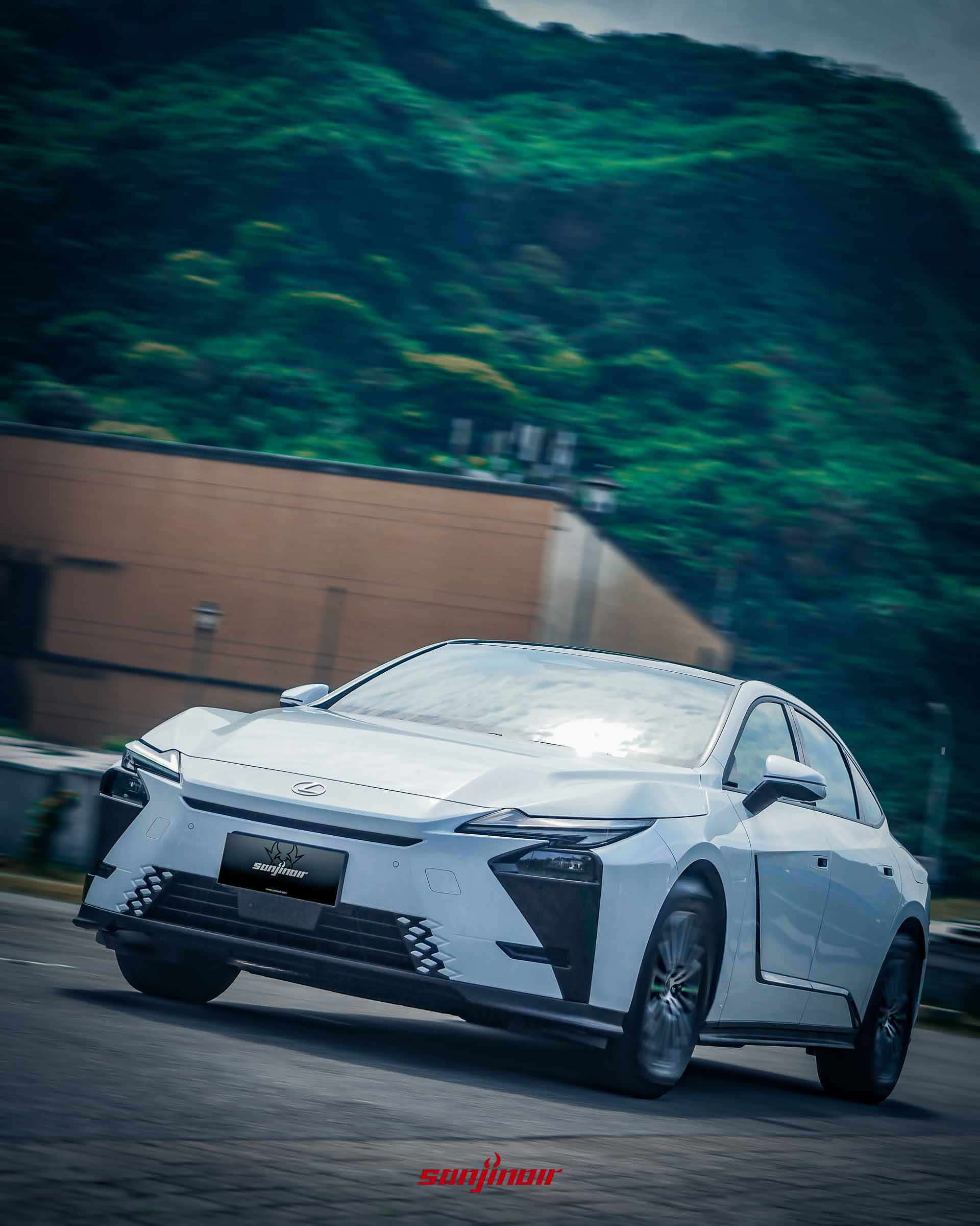 白色Lexus ES 300h在道路上行駛的動態追焦照,背景為模糊的綠色山林與建築物。