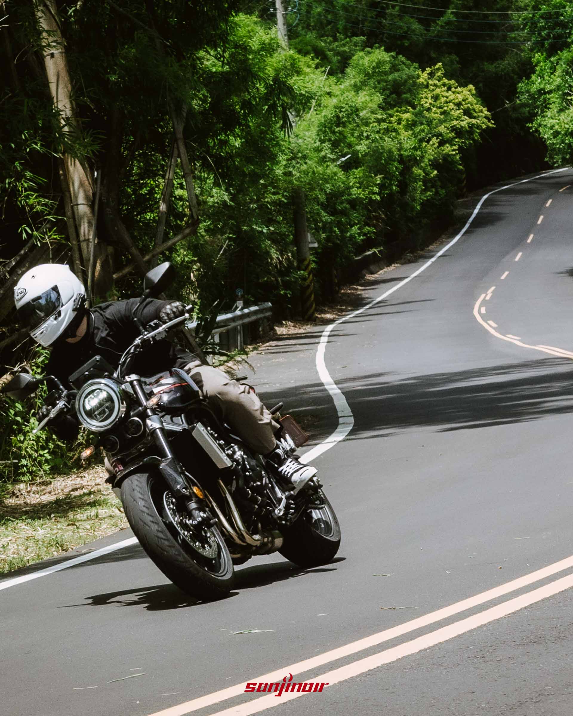 騎士騎乘Honda CB1000F在蜿蜒的柏油山路上向左壓車過彎的正面動態追焦照片。