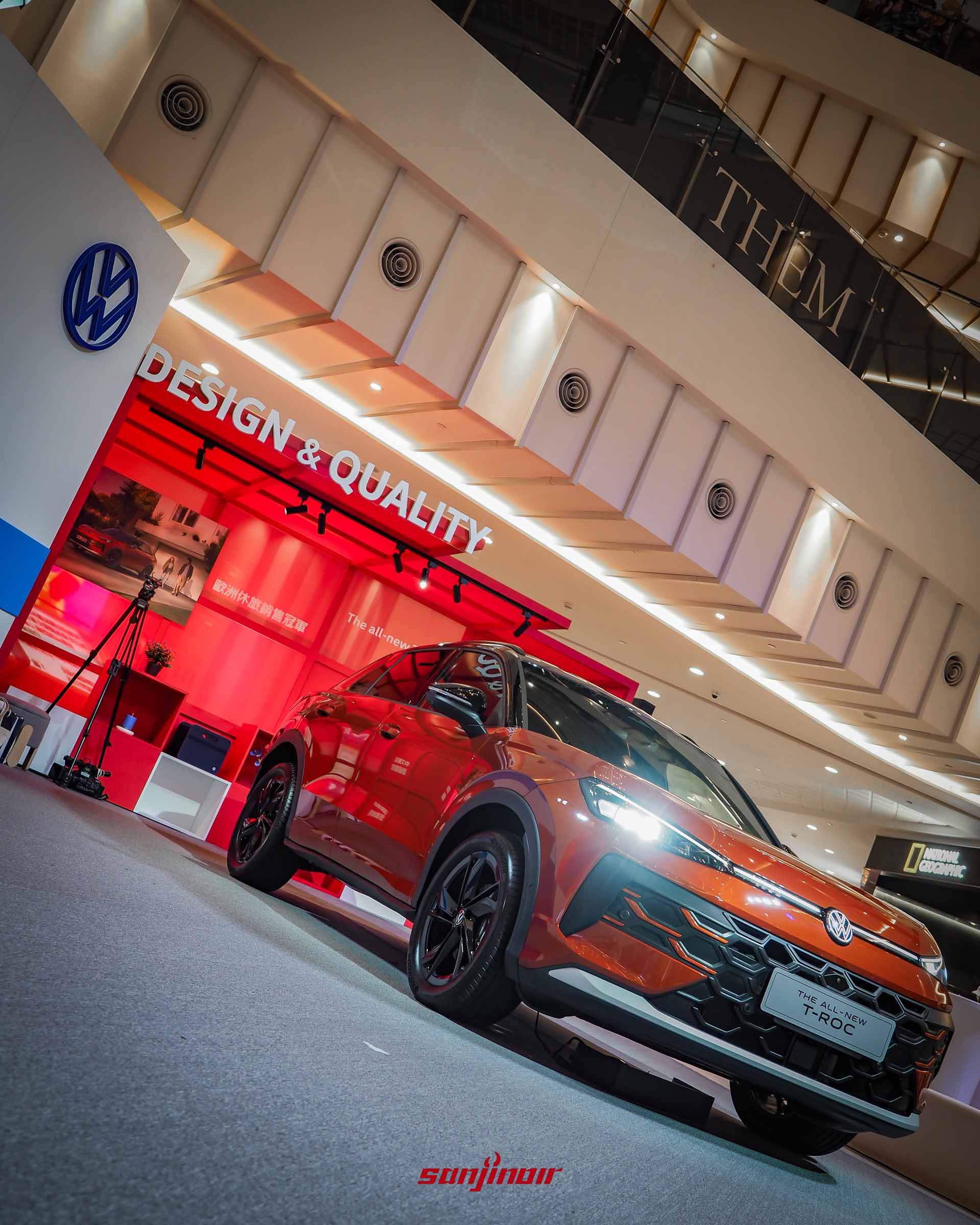 由低角度拍攝的赤焰紅色Volkswagen T-Roc極夜曜影版正面與側面視角,配備黑化輪圈與飾條,背景有「DESIGN & QUALITY」的紅色展示看板。