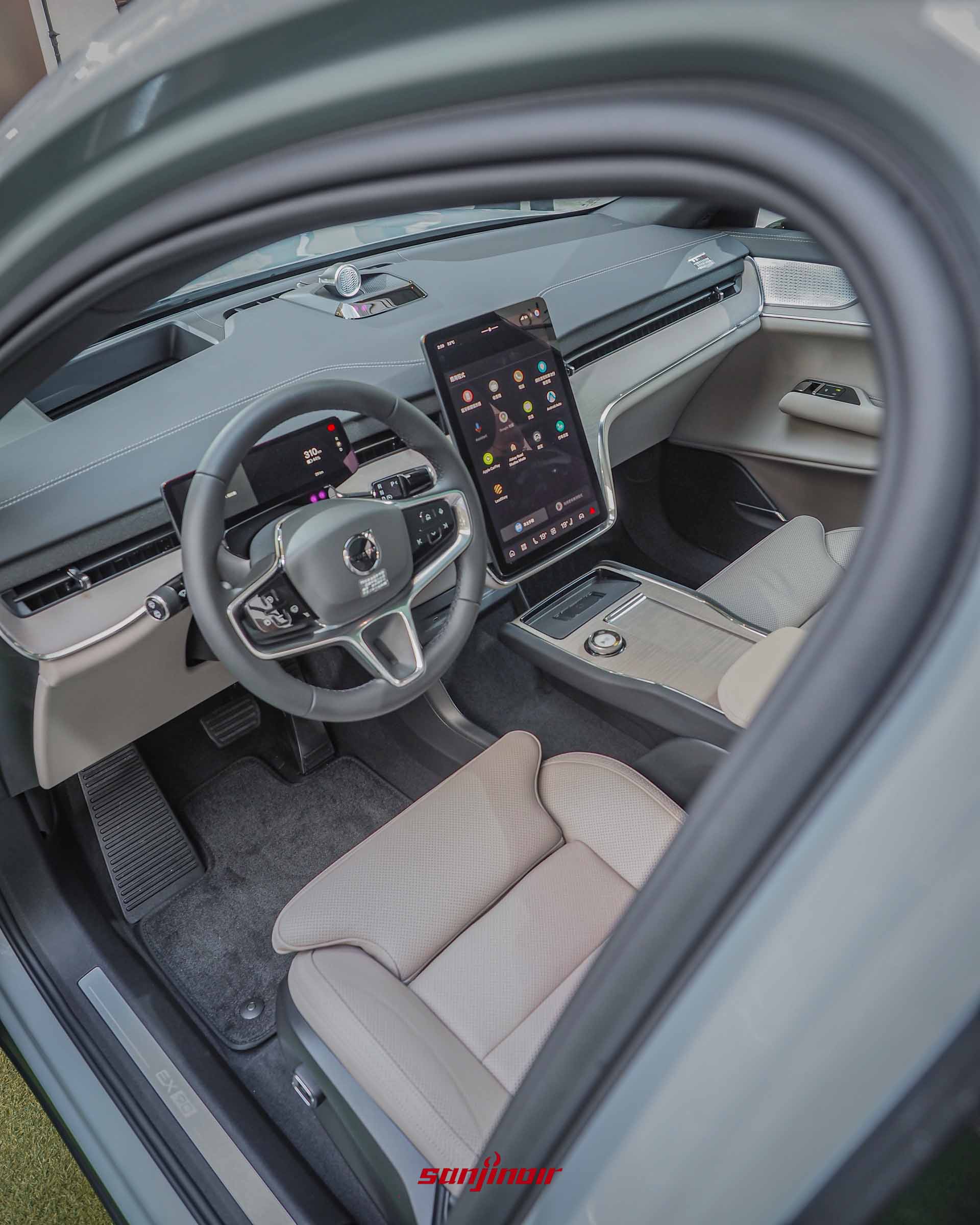 從車外望入Volvo EX90的駕駛座艙,可見方向盤、前方的數位儀表板、中央的大型直立式觸控螢幕以及帶有精緻旋鈕的簡約中央扶手。