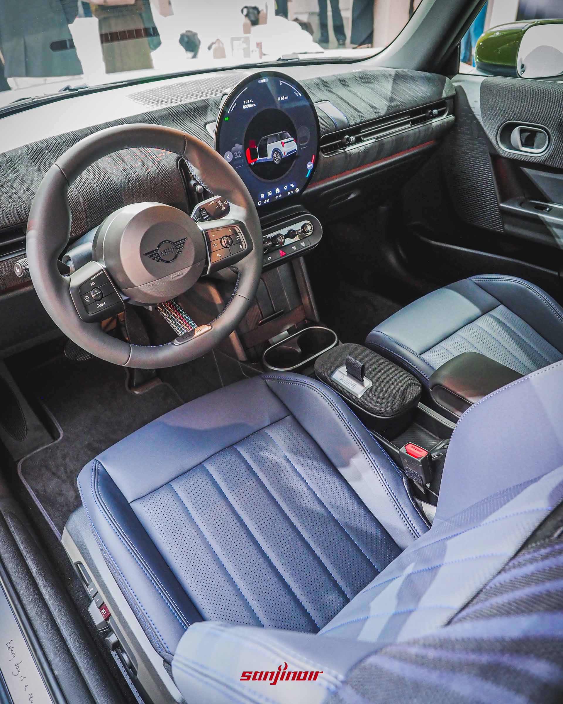 MINI特仕車的駕駛座艙全景，包含駕駛座跑車座椅、方向盤、中央懸浮式大型圓形螢幕，以及藍色與黑色相間的皮布拼接內裝材質。