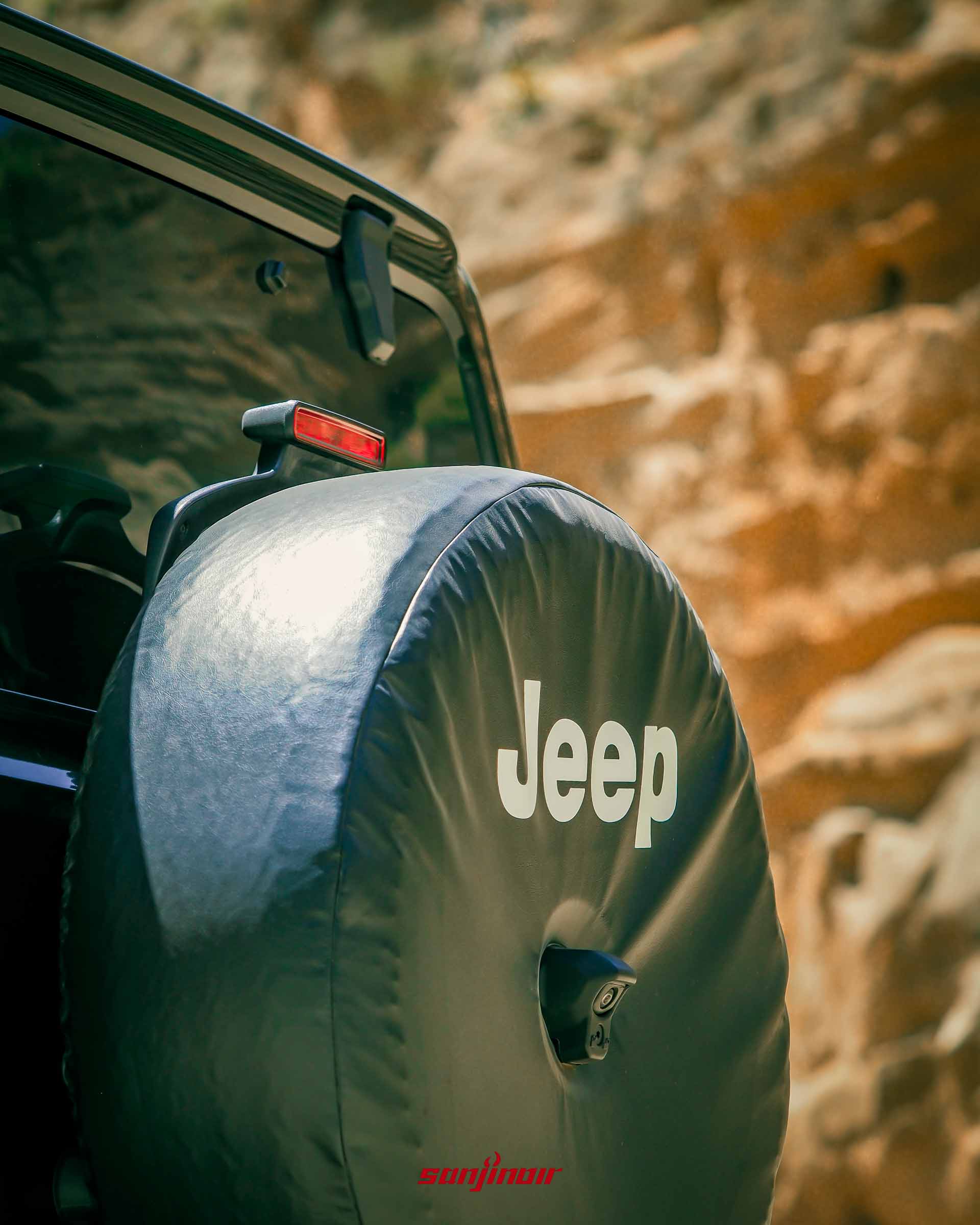 Jeep Wrangler Sahara 車尾的備胎特寫,備胎套上有白色的 Jeep 字樣,下方有倒車顯影鏡頭。