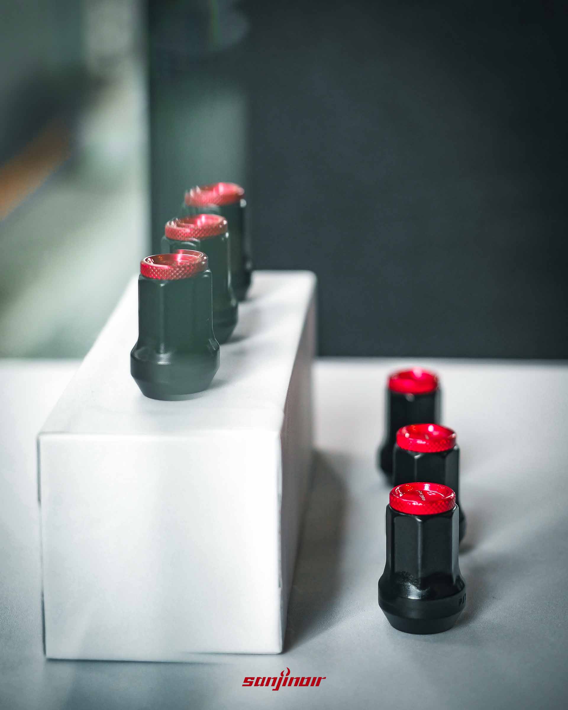 擺放在白色展示台上的 AutoExe 高剛性防盜螺帽，側寫凸顯其耐高溫鉻釩鋼黑色本體與紅色陽極端蓋的精緻工藝。