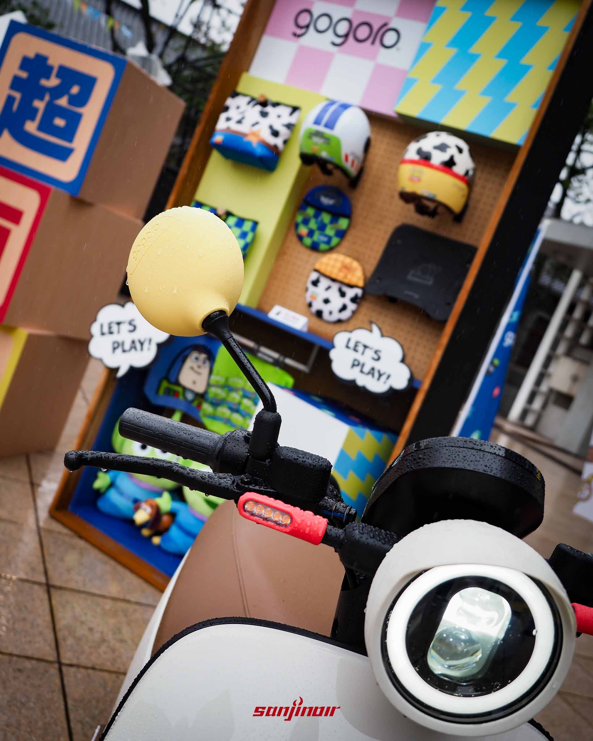 從騎士視角拍攝的Gogoro機車龍頭，配有黃色後照鏡矽膠套，背景為安全帽展示牆。