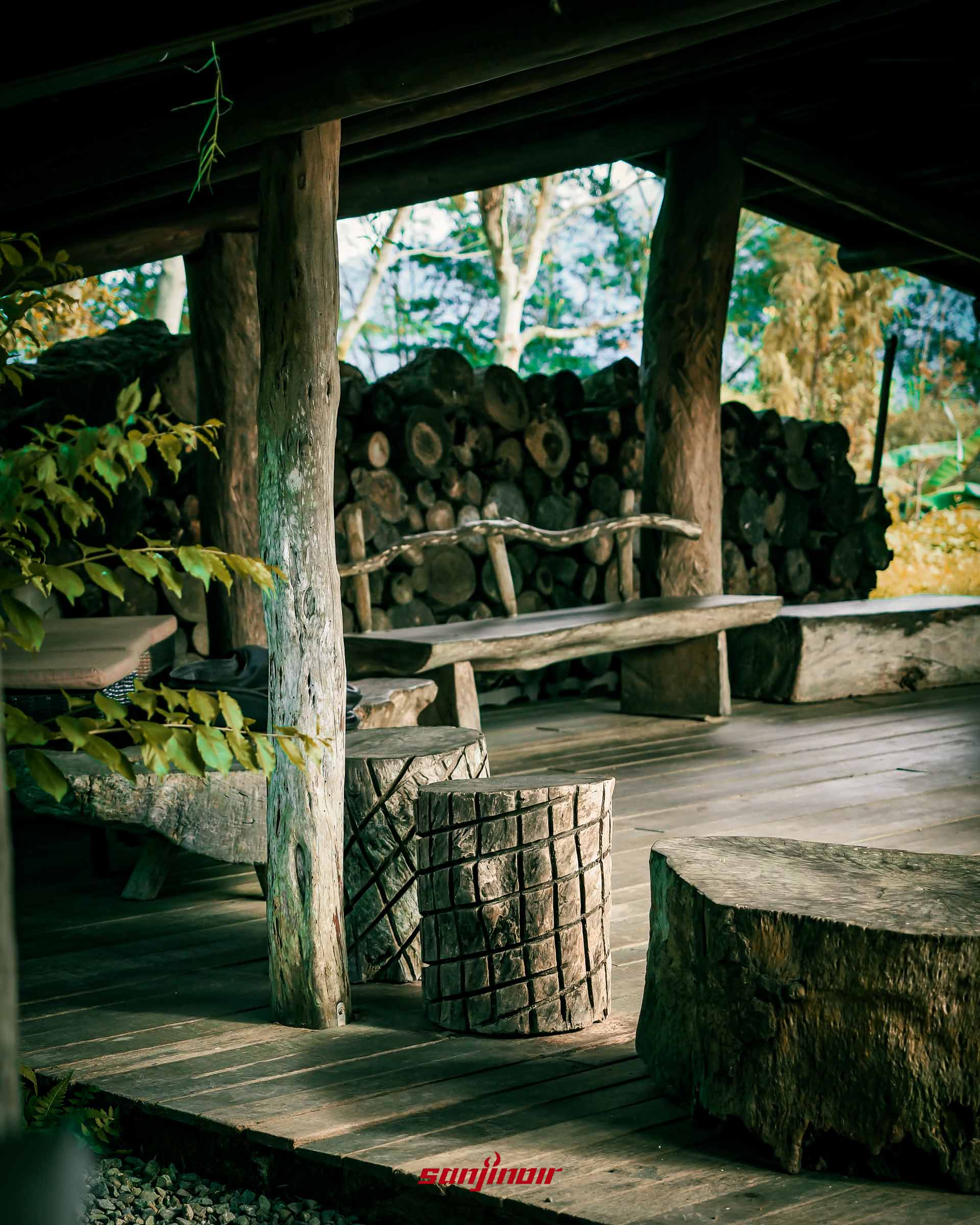 茅草屋內部視角粗壯木柱與刻有紋路木樁座椅背景堆滿柴火。