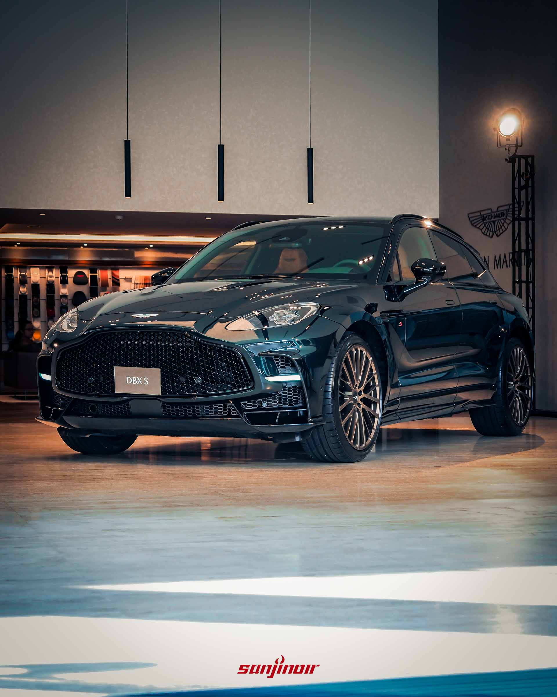 一輛深綠色 Aston Martin DBX S 高性能休旅車，正側面視角，停在展場中，展示其具侵略性的車身包圍和大尺寸鍛造輪圈。