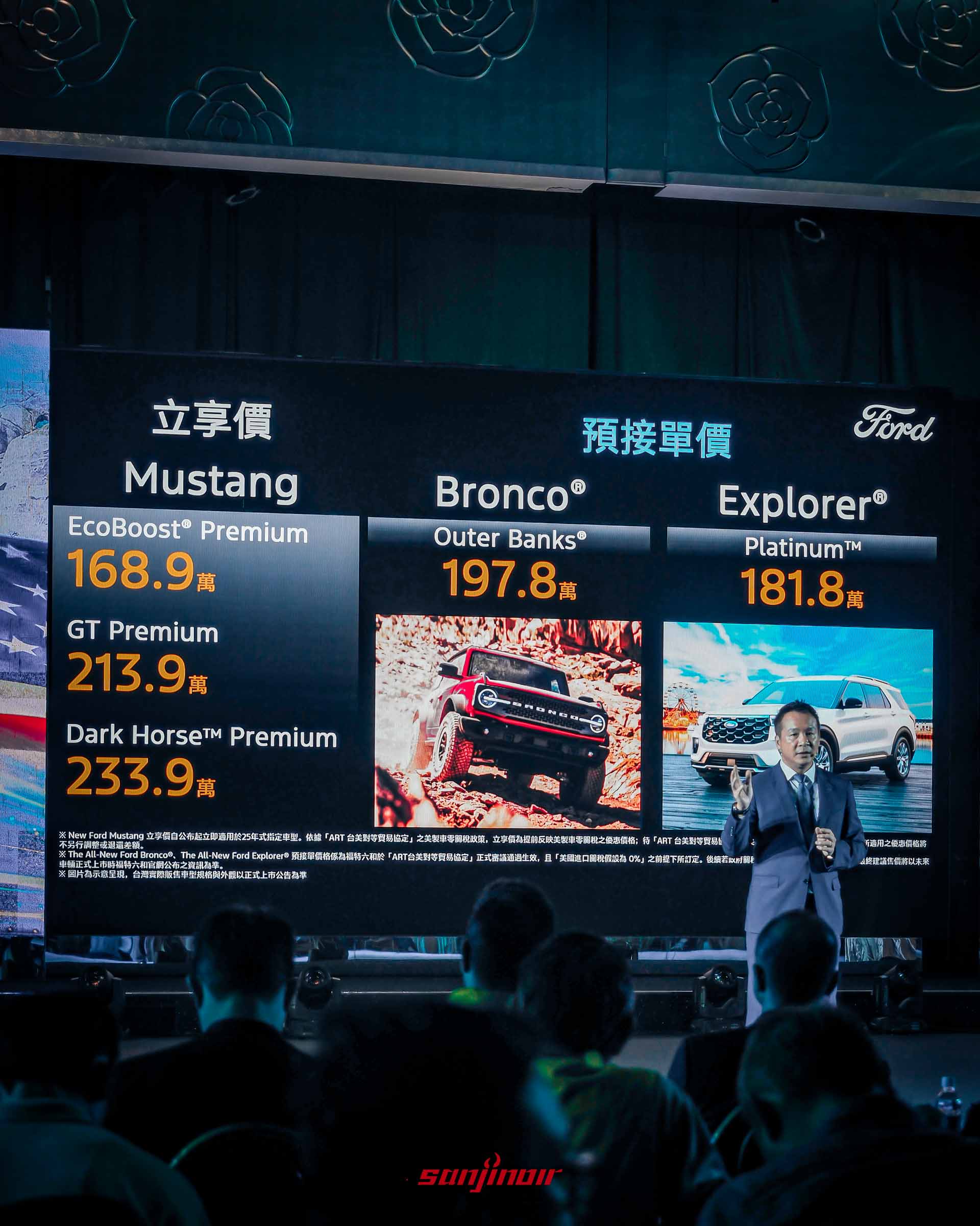 發表會現場遠景。大螢幕上清晰顯示「立享價 Mustang TWD 1,689,000」、「預接單價 Bronco® Outer Banks® TWD 1,978,000」、「預接單價 Explorer® Platinum™ TWD 1,818,000」字樣，並有Bronco和Explorer的圖片。