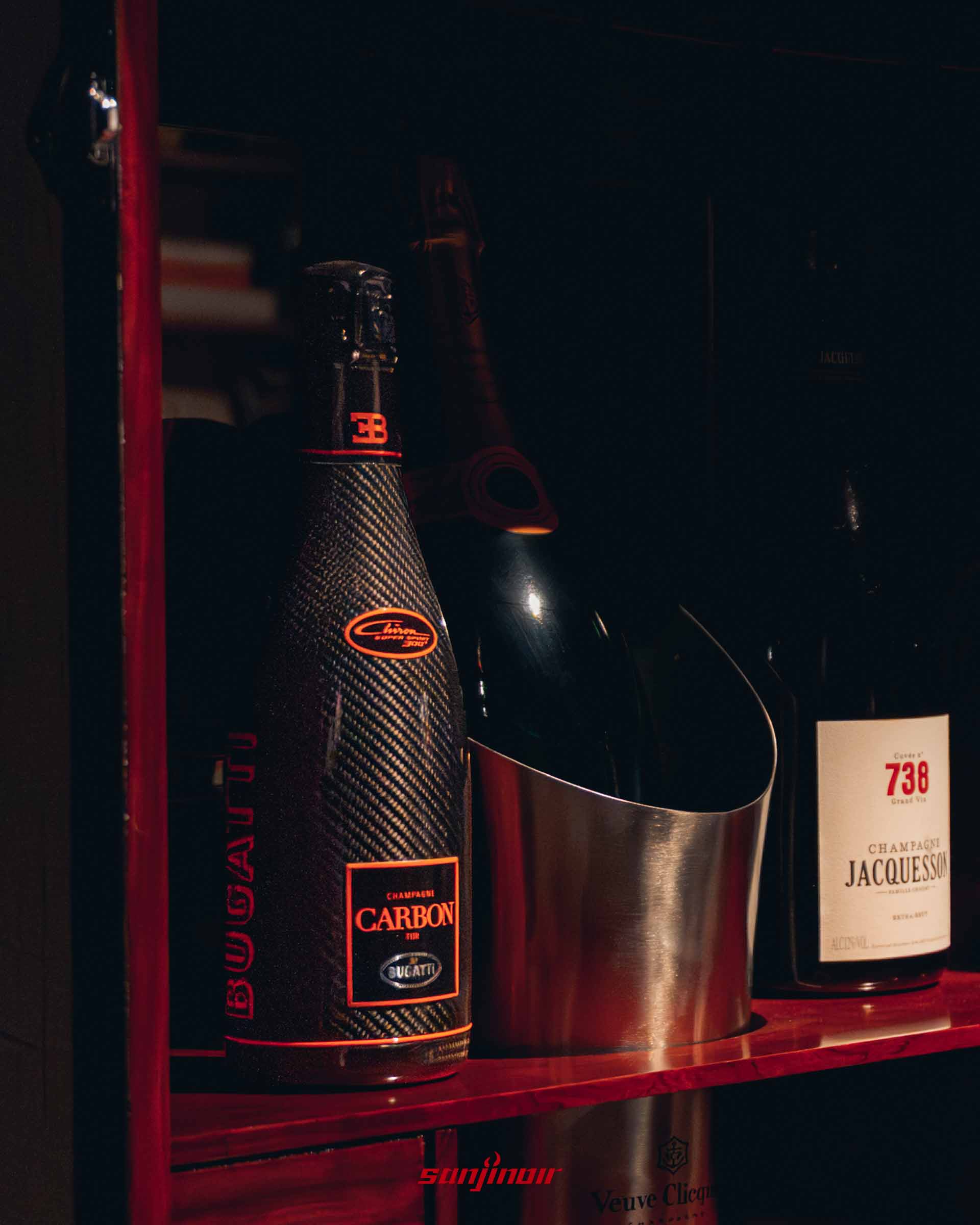 特製酒櫃中擺放著一瓶碳纖維瓶身的 Bugatti Carbon 香檳，旁邊附有金屬冰桶與其他頂級酒款。