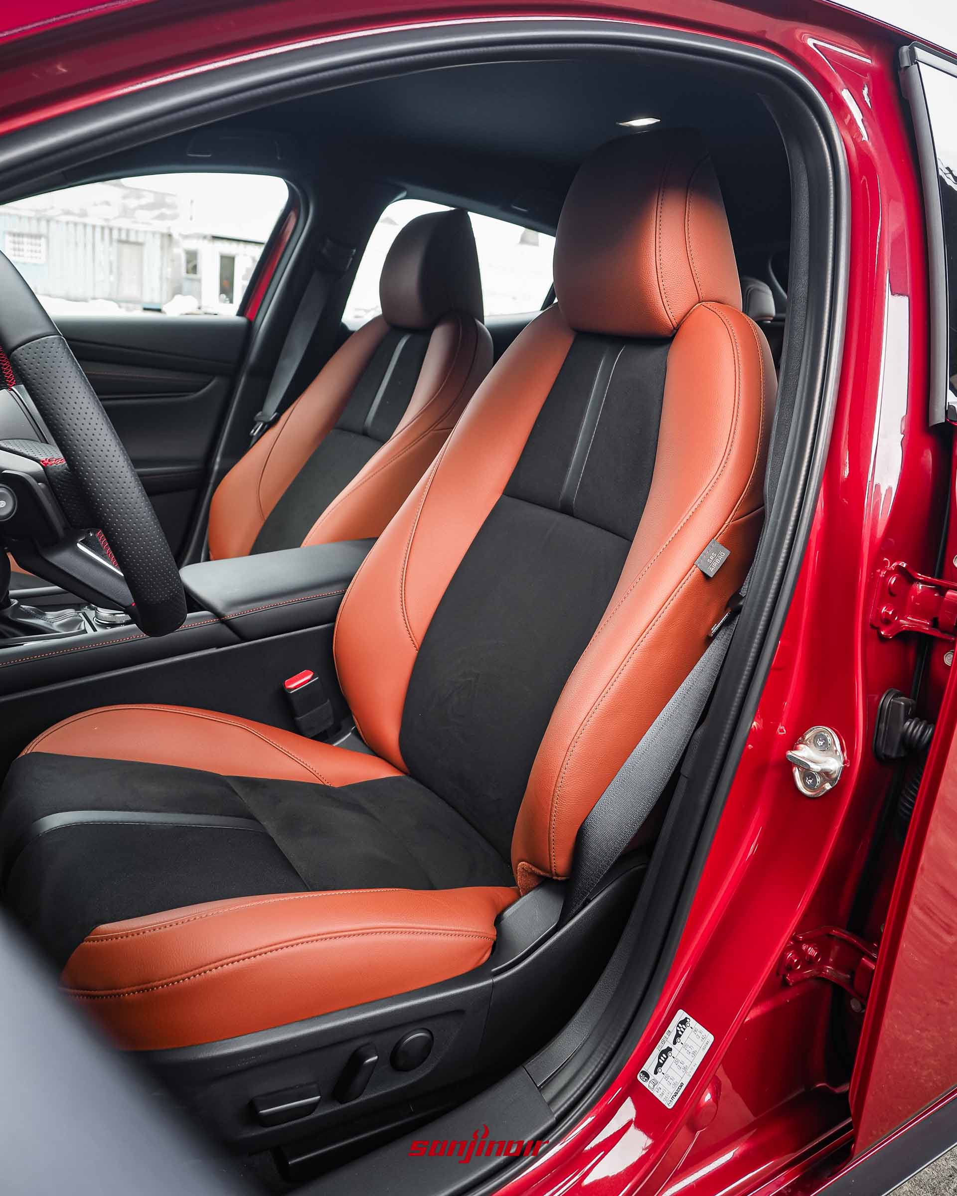 從開著門的駕駛側拍攝MAZDA3 HOMURA內裝，赤陶紅和黑色麂皮座椅清晰，可以看到方向盤和排檔頭。