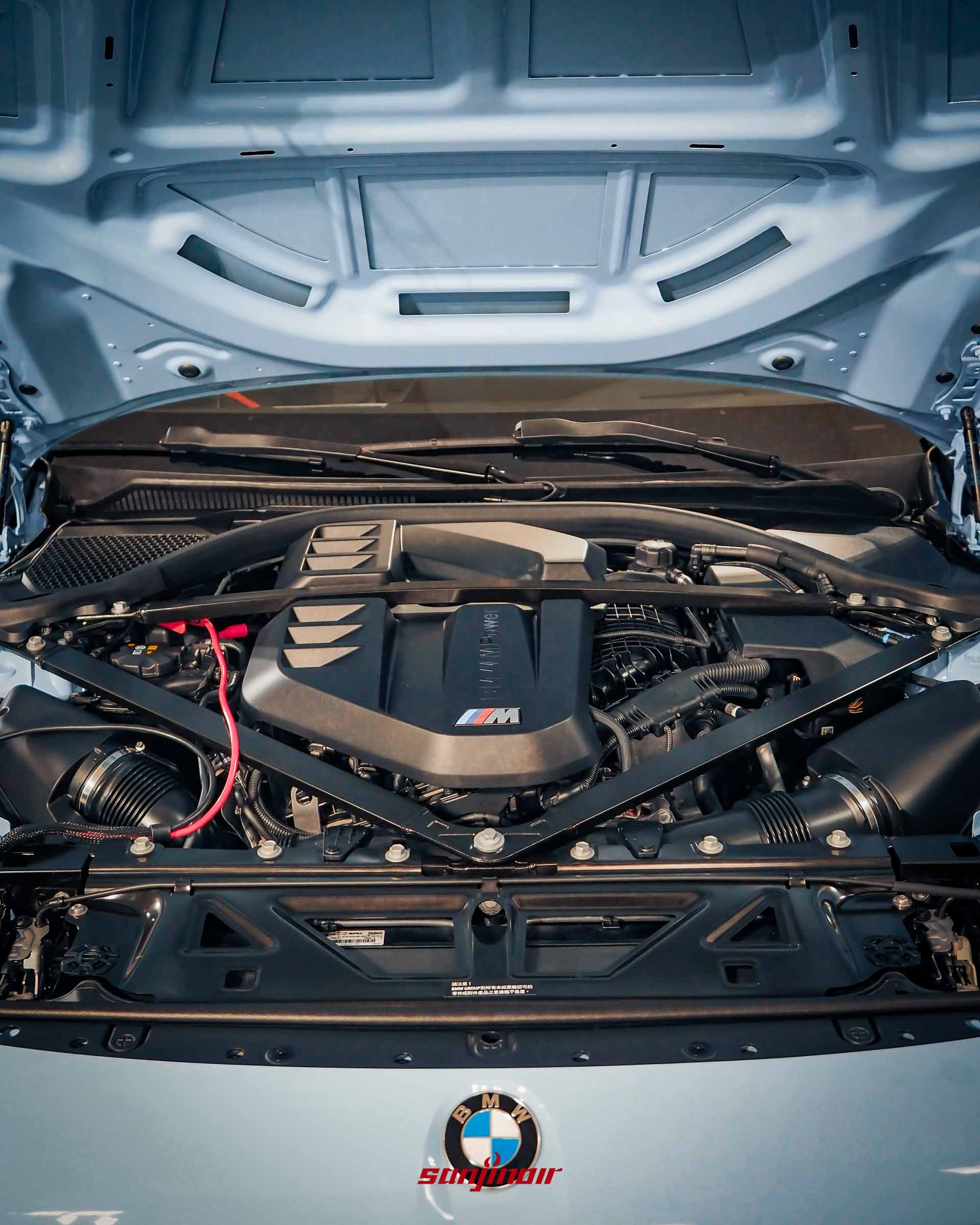 BMW M2打開引擎蓋的引擎室特寫照，展示直列六缸引擎與上方M Power字樣護蓋，車身烤漆為淺藍色。