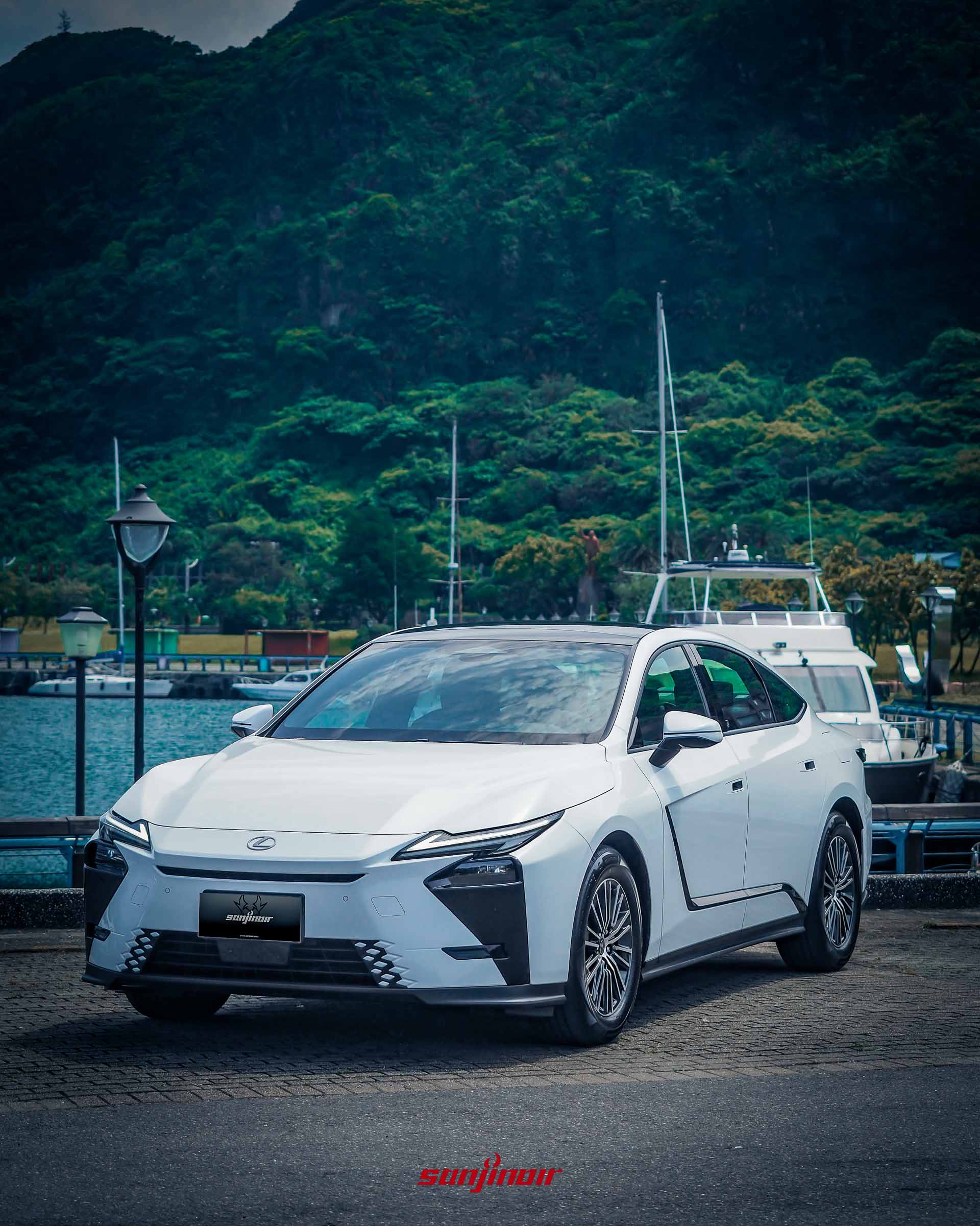 直式構圖的白色Lexus ES 300h前側方視角,停駐於綠意盎然的山脈與遊艇碼頭前。