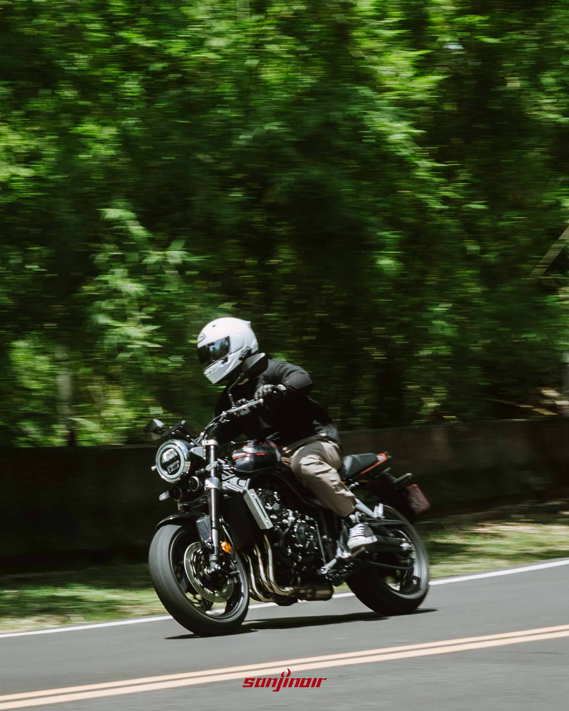 騎士騎乘Honda CB1000F在山道上快速行駛的側面動態追焦照片,背景綠樹呈現速度模糊感。