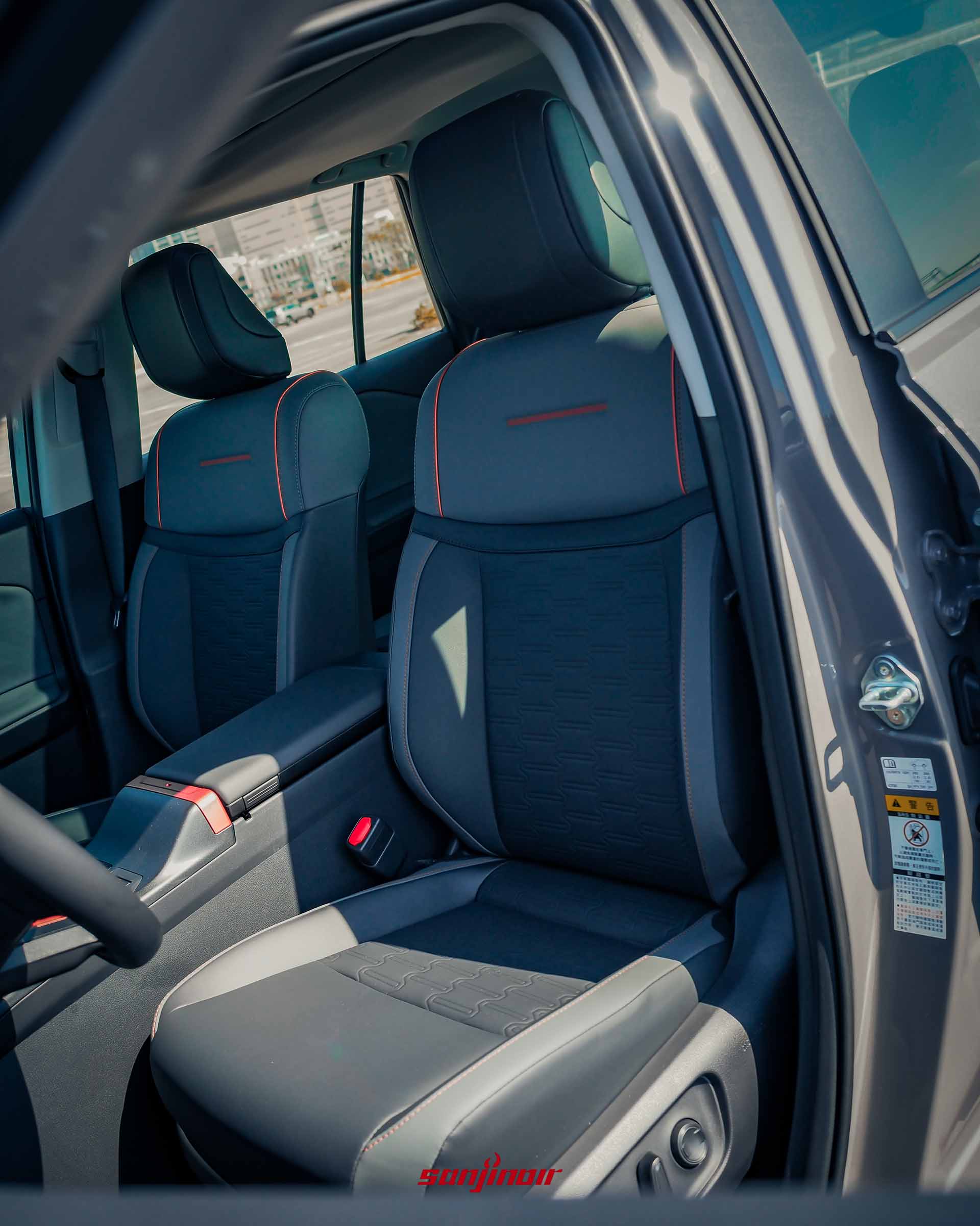 駕駛座座椅特寫，展示黑色皮革、橘色滾邊與幾何壓紋細節。