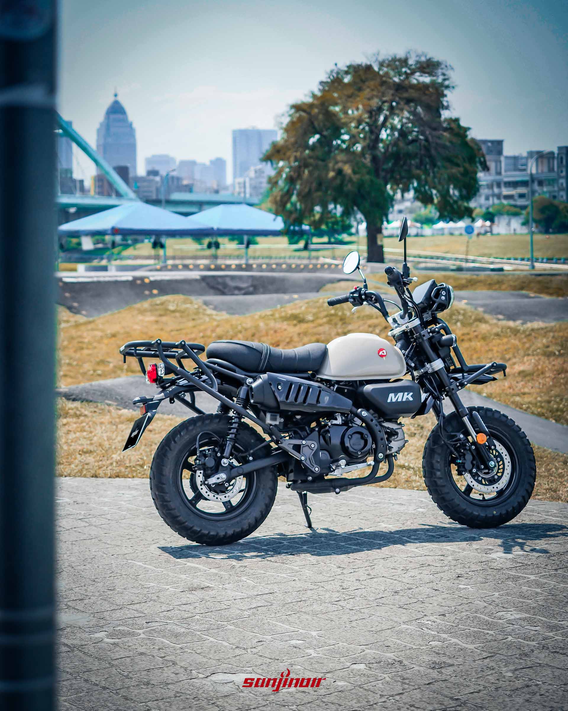 Aeontek MK150右後方視角停放於公園，清楚呈現高挺的排氣管尾段與充滿曠野氣息的巧克力胎。